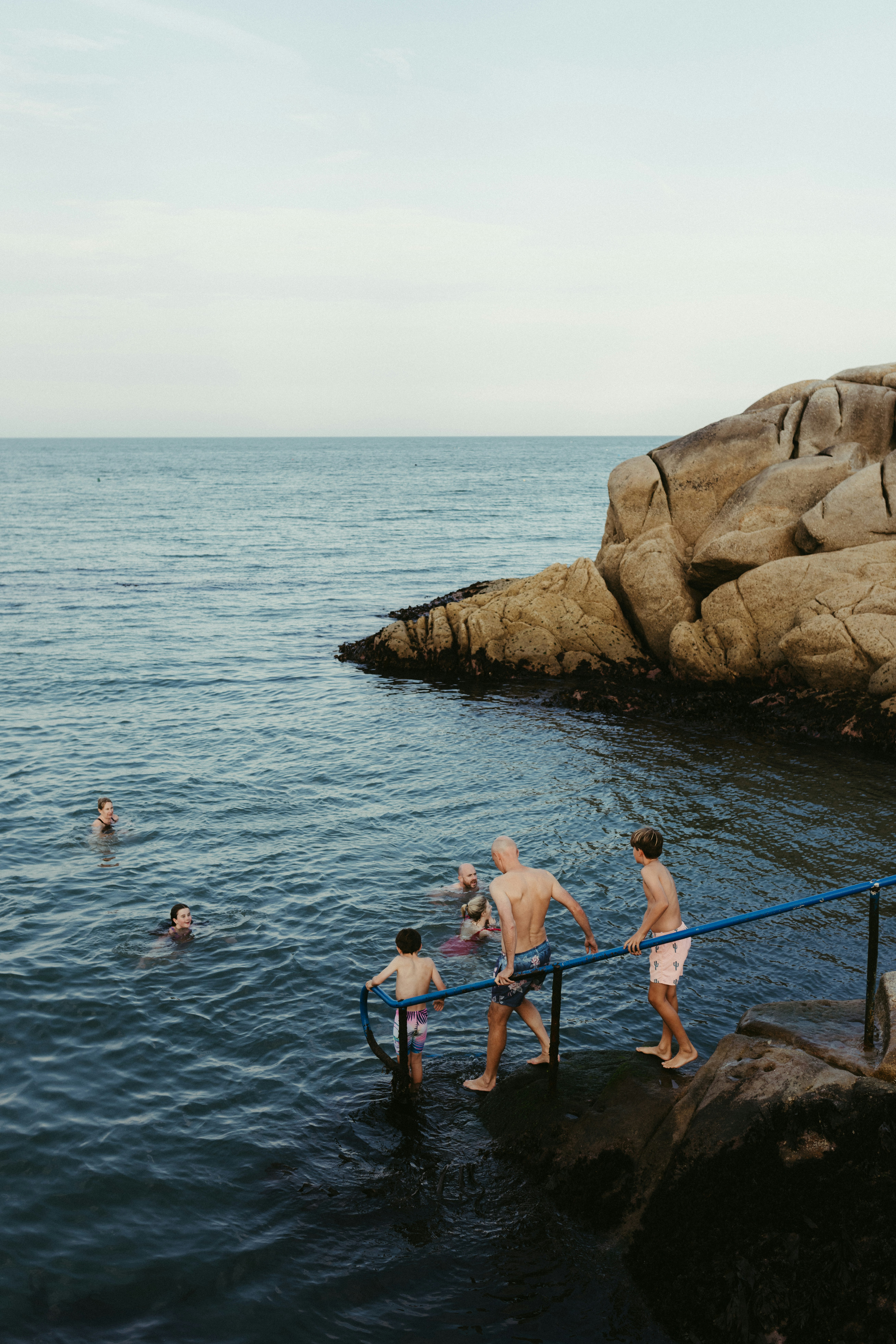 People swimming in ocean near rocky shore.