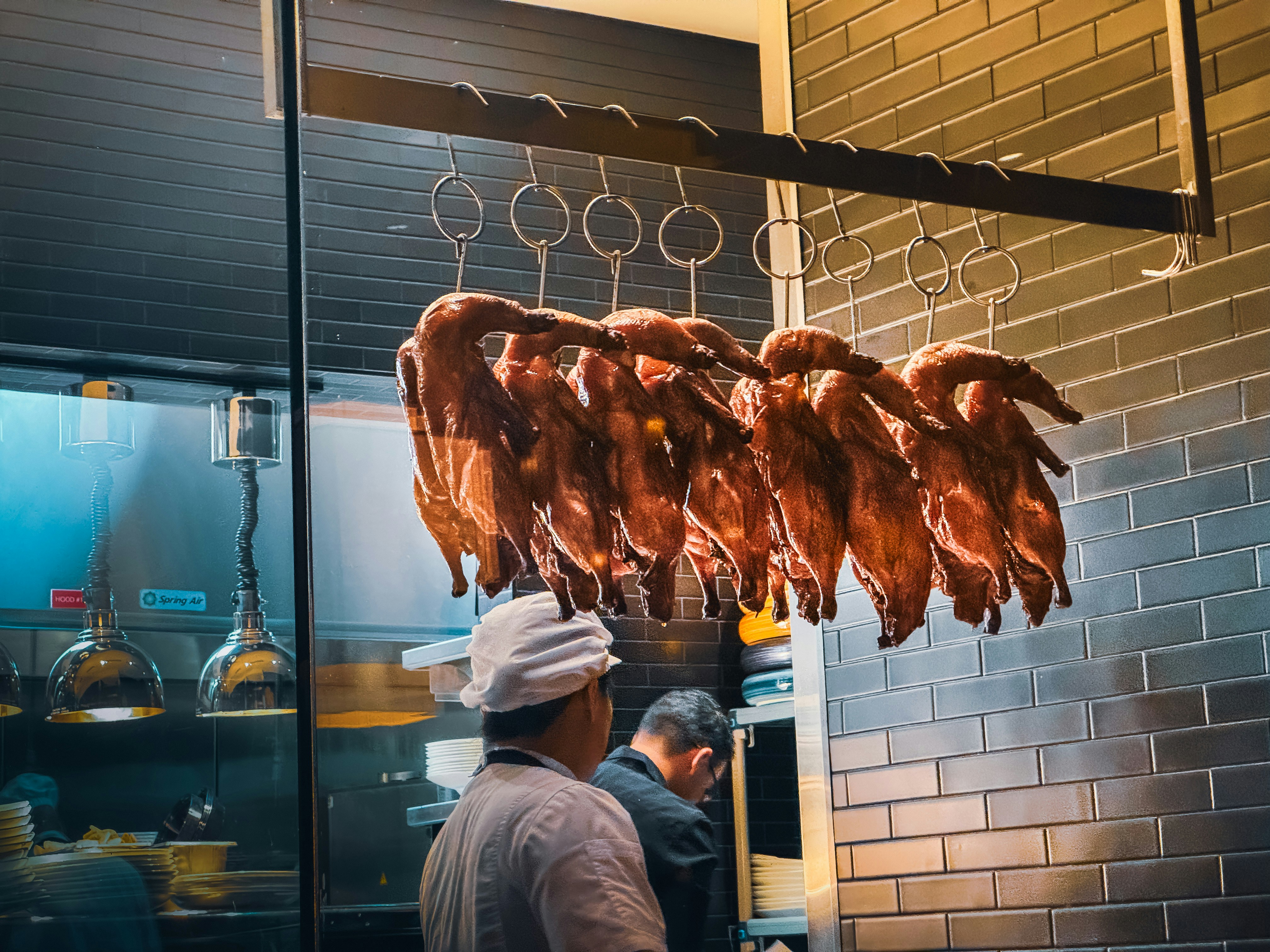 Several roasted ducks hanging in a restaurant kitchen.