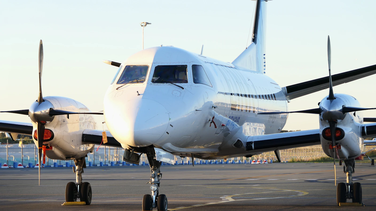 A white twin-engine turboprop aircraft parked on an airport apron