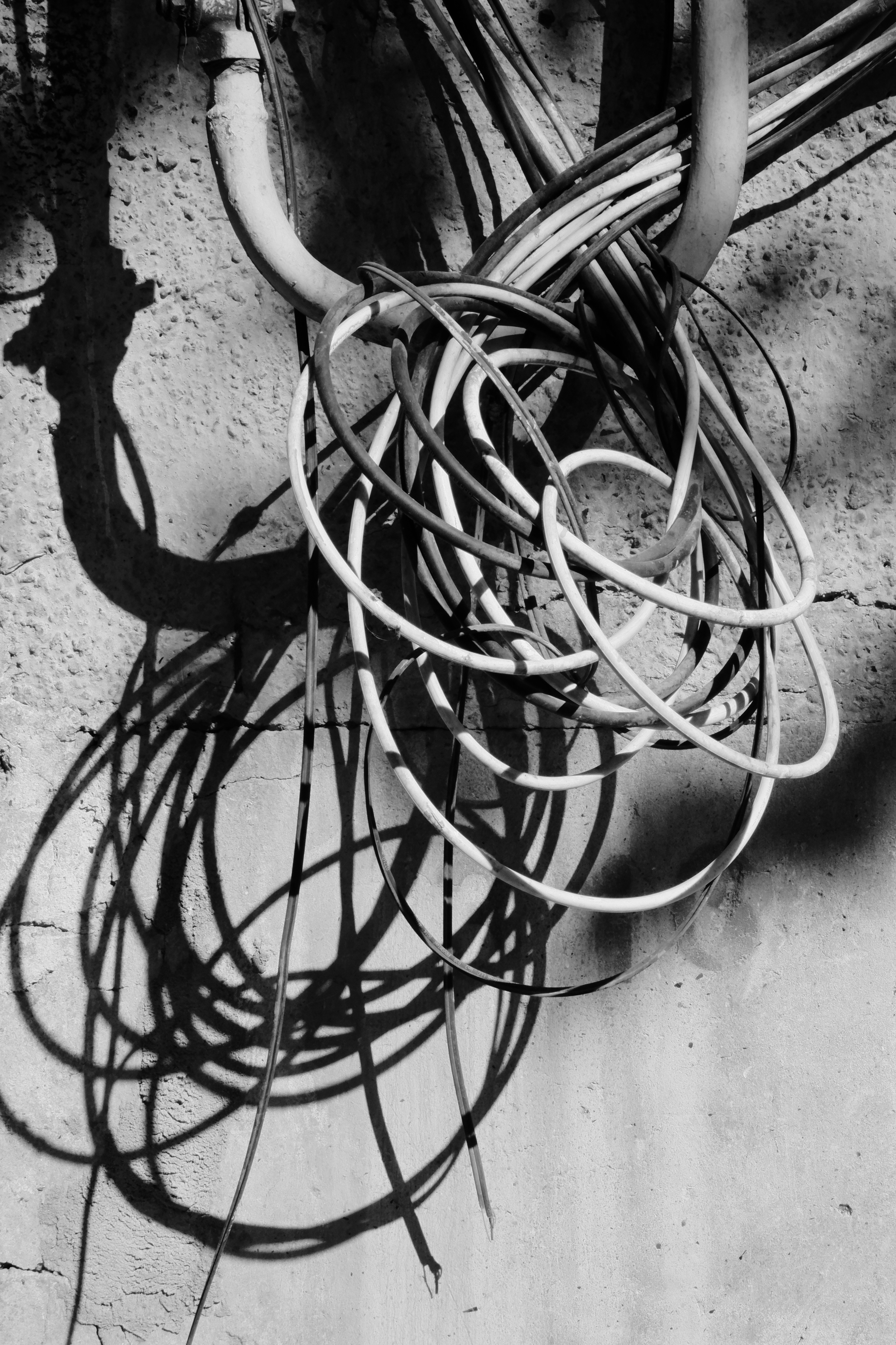 Tangled electrical wires casting shadows on a textured wall.