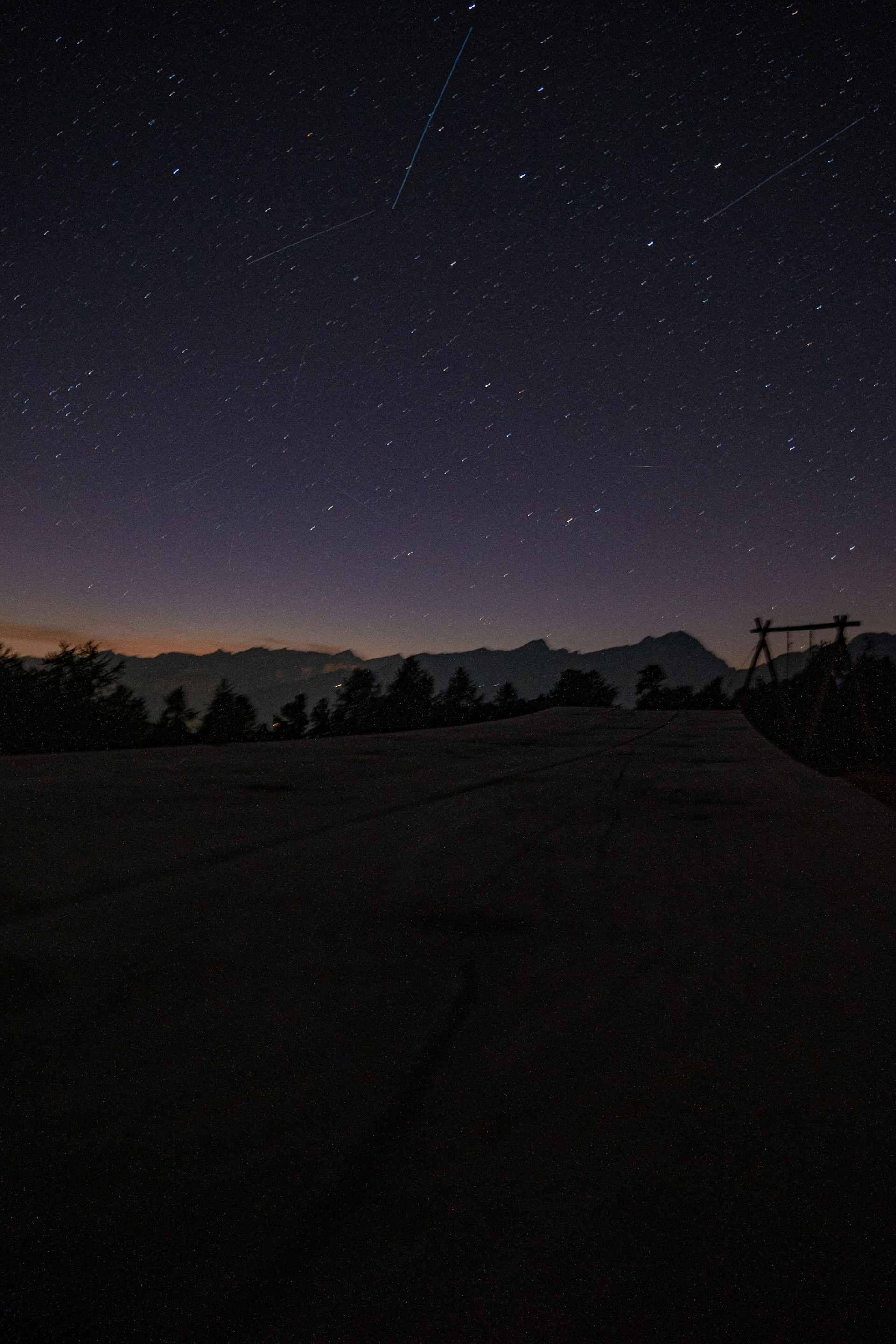 Starry night sky over silhouetted mountains and trees