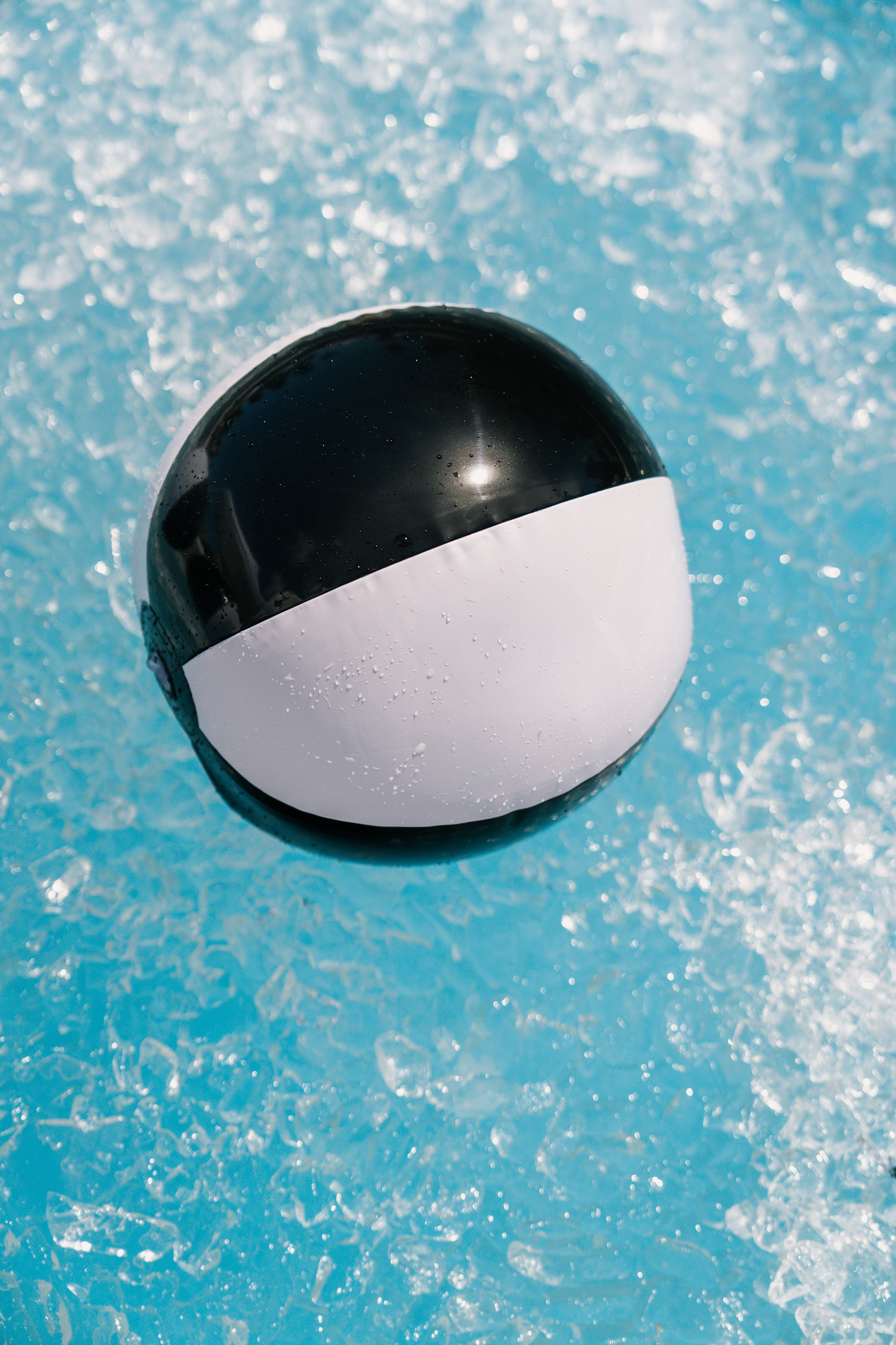 A black and white ball floats on blue water.