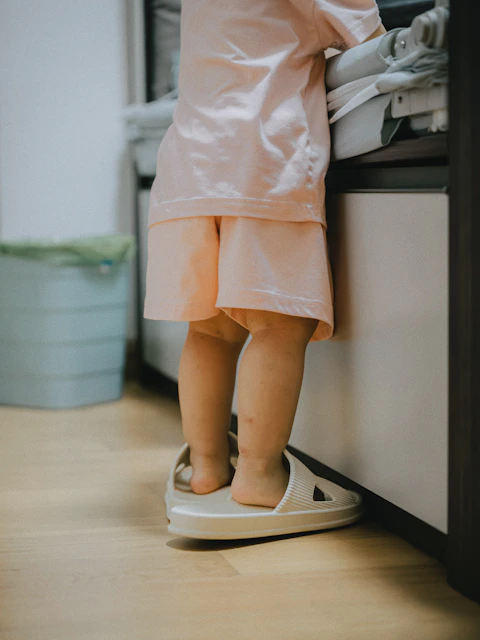 Toddler wearing oversized slippers stands by counter.