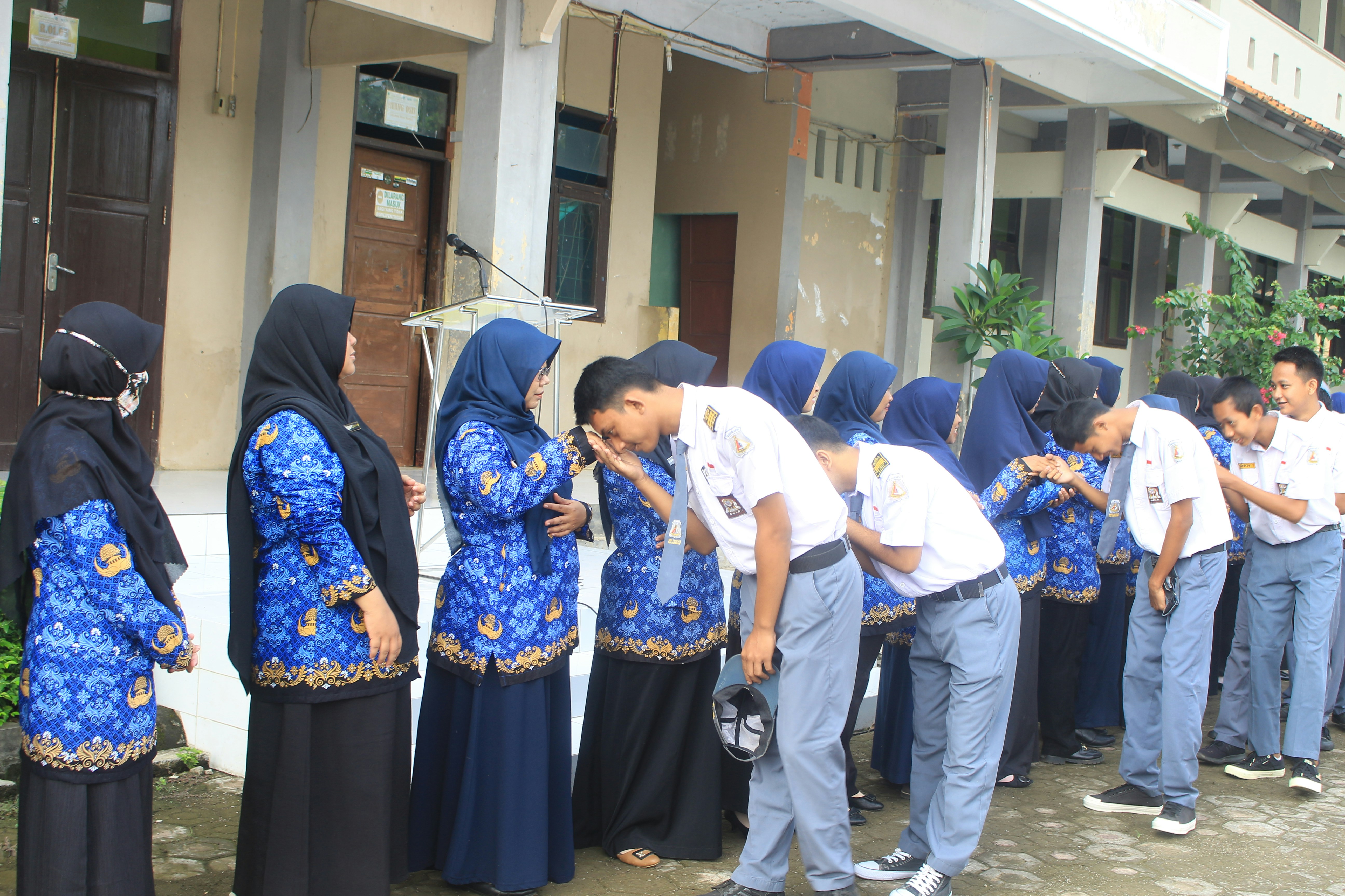 Des élèves s’inclinent devant des enseignants à l’extérieur d’un bâtiment.