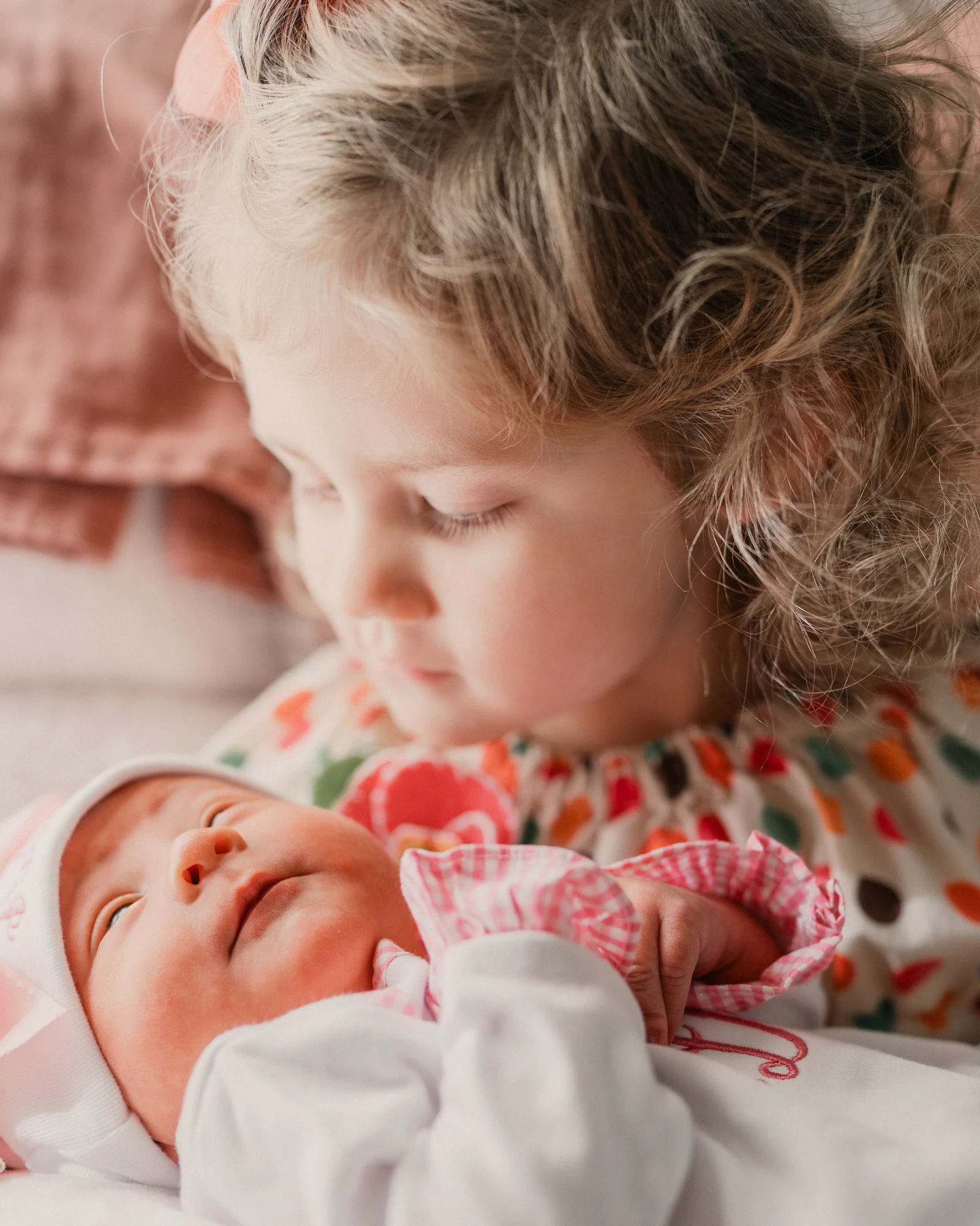 An older sister looks closely at her newborn sibling while the family prepares a child for a new sibling