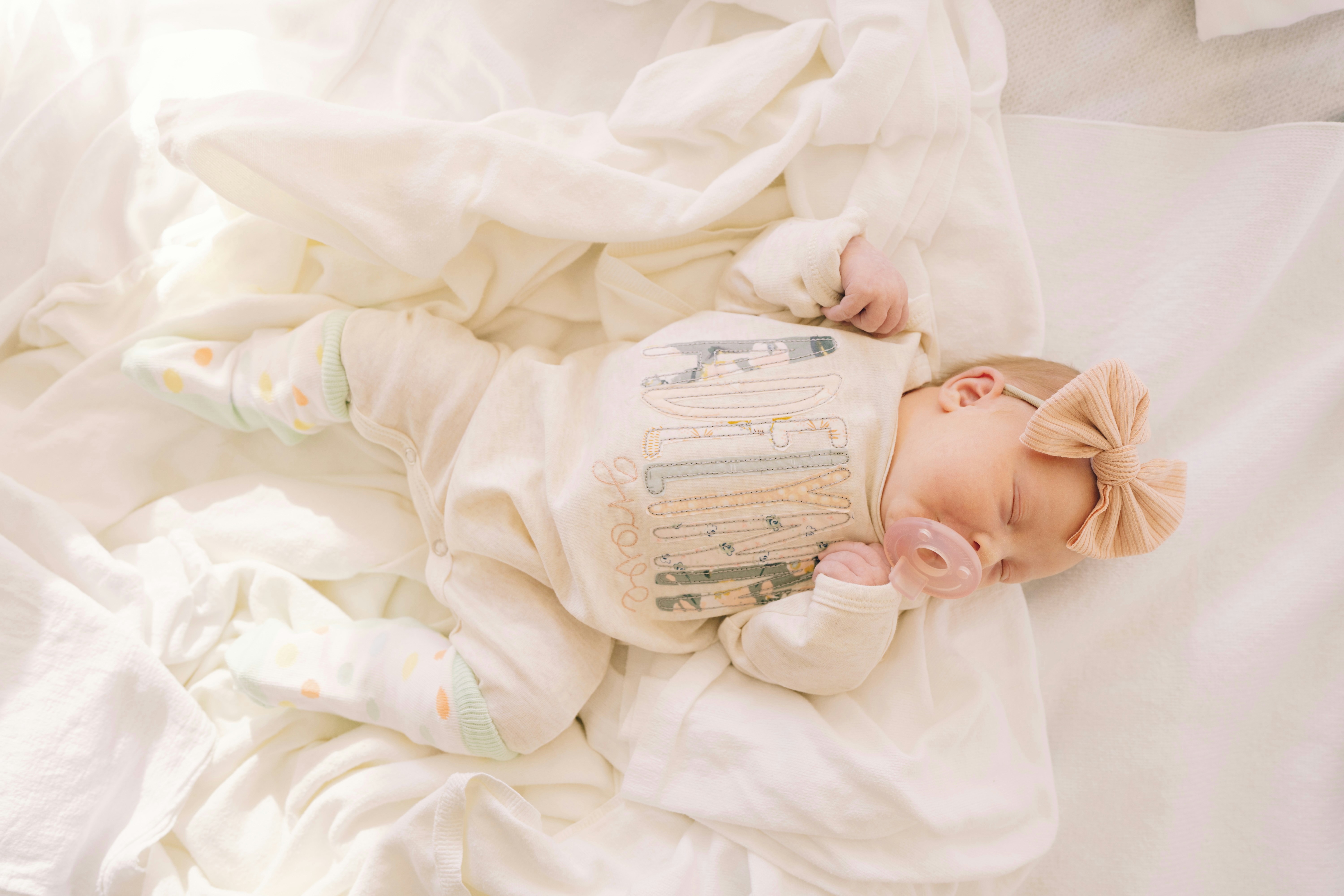 A newborn baby sleeps peacefully on a white blanket.