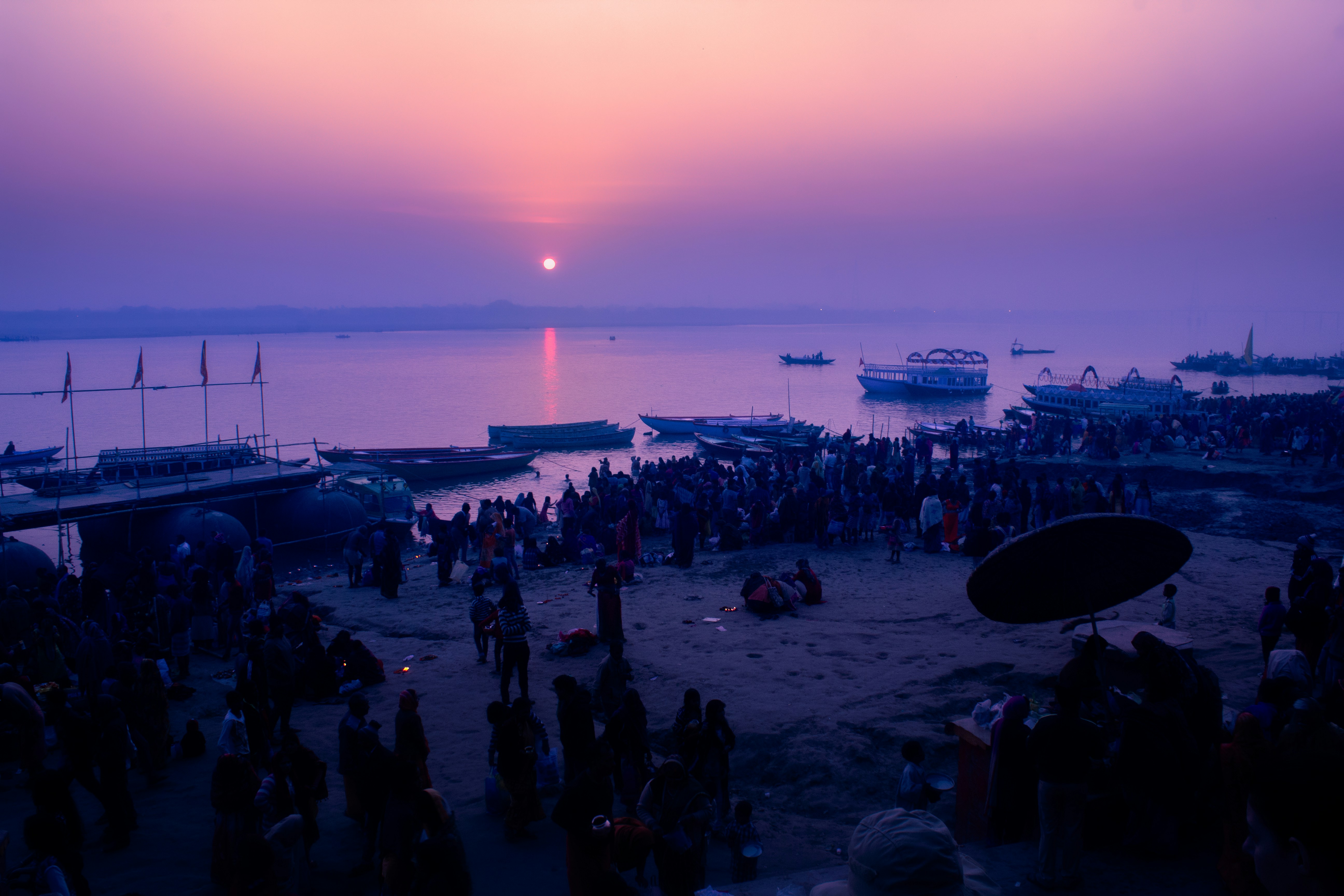 Sunrise over a crowded riverbank with boats.