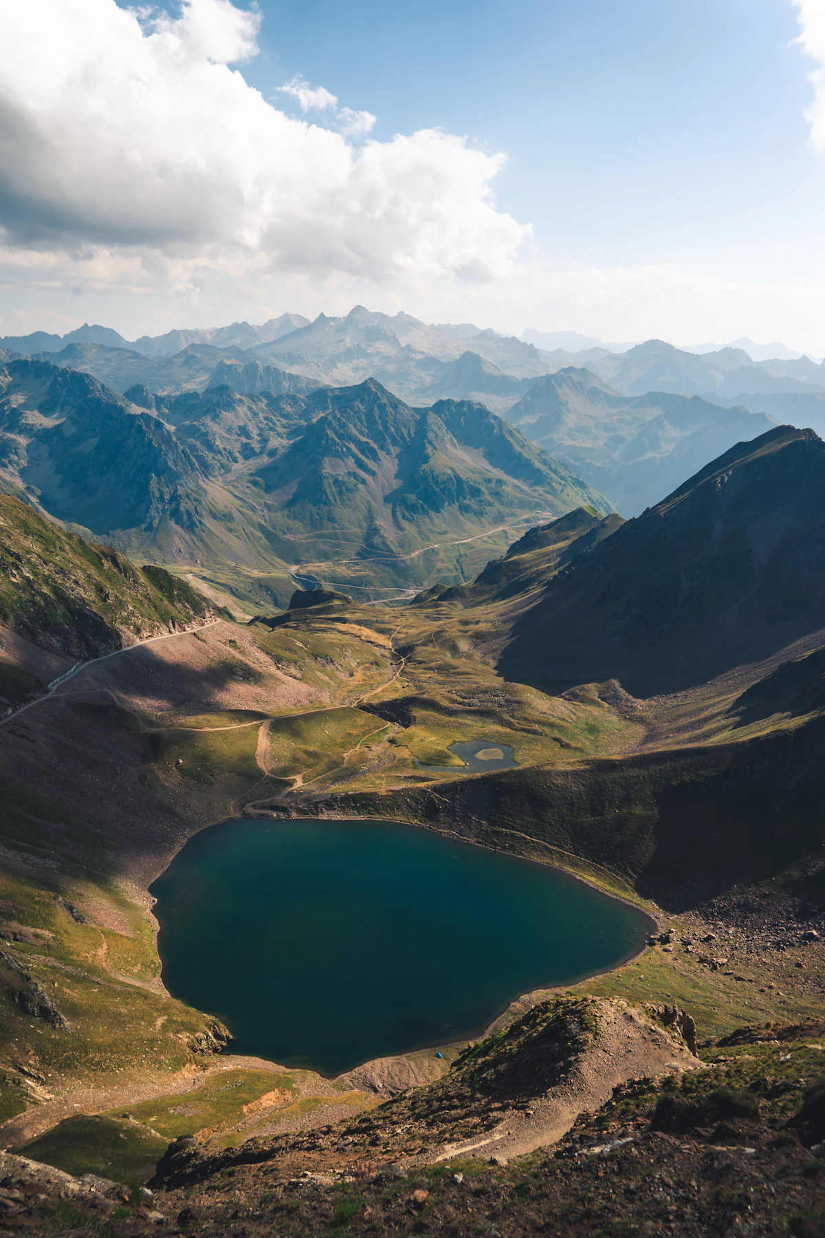 A deep blue lake in a green bowl below the Pic du Midi de Bigorre, with tracks winding across the slope