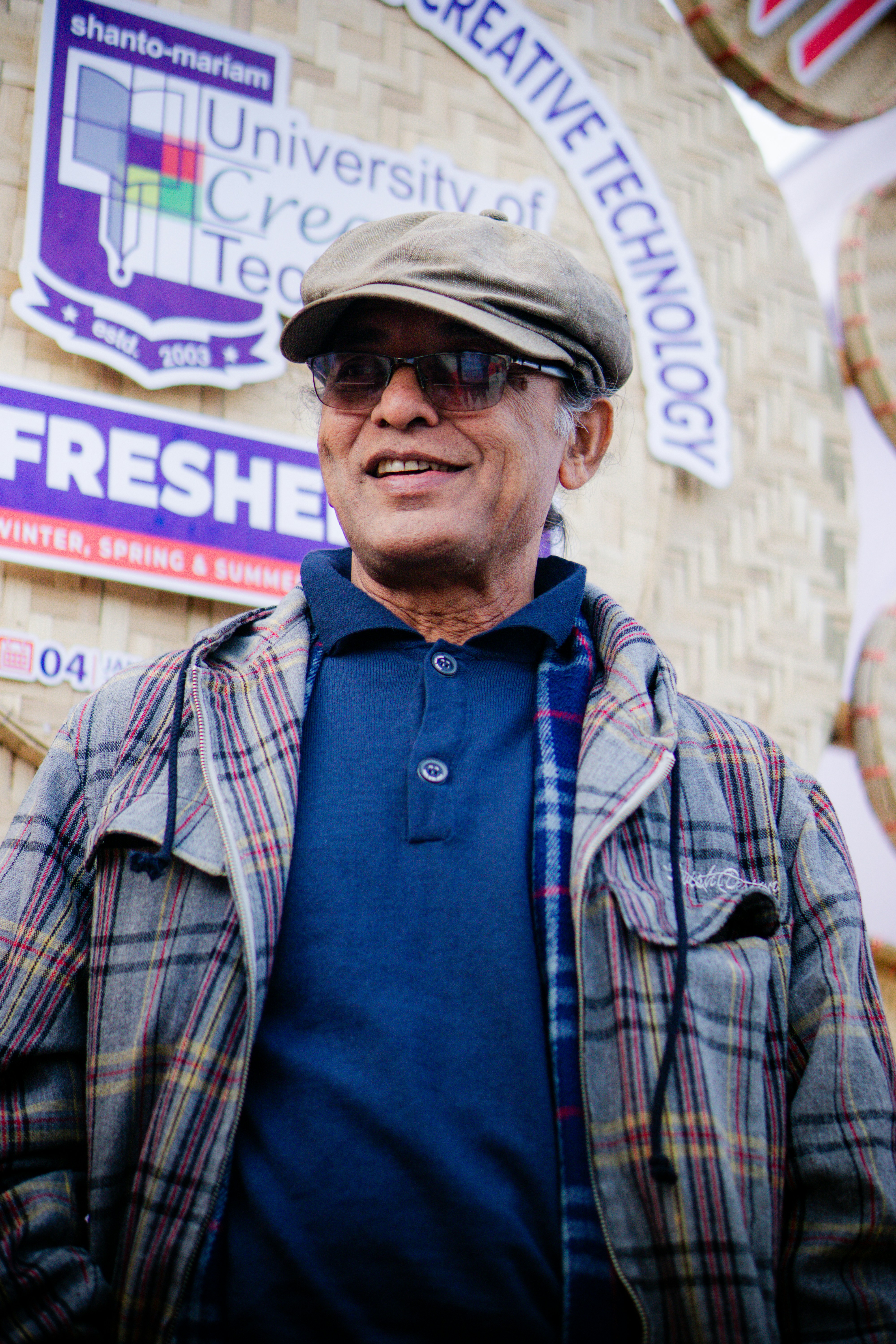 An older man wearing a cap and glasses smiles.