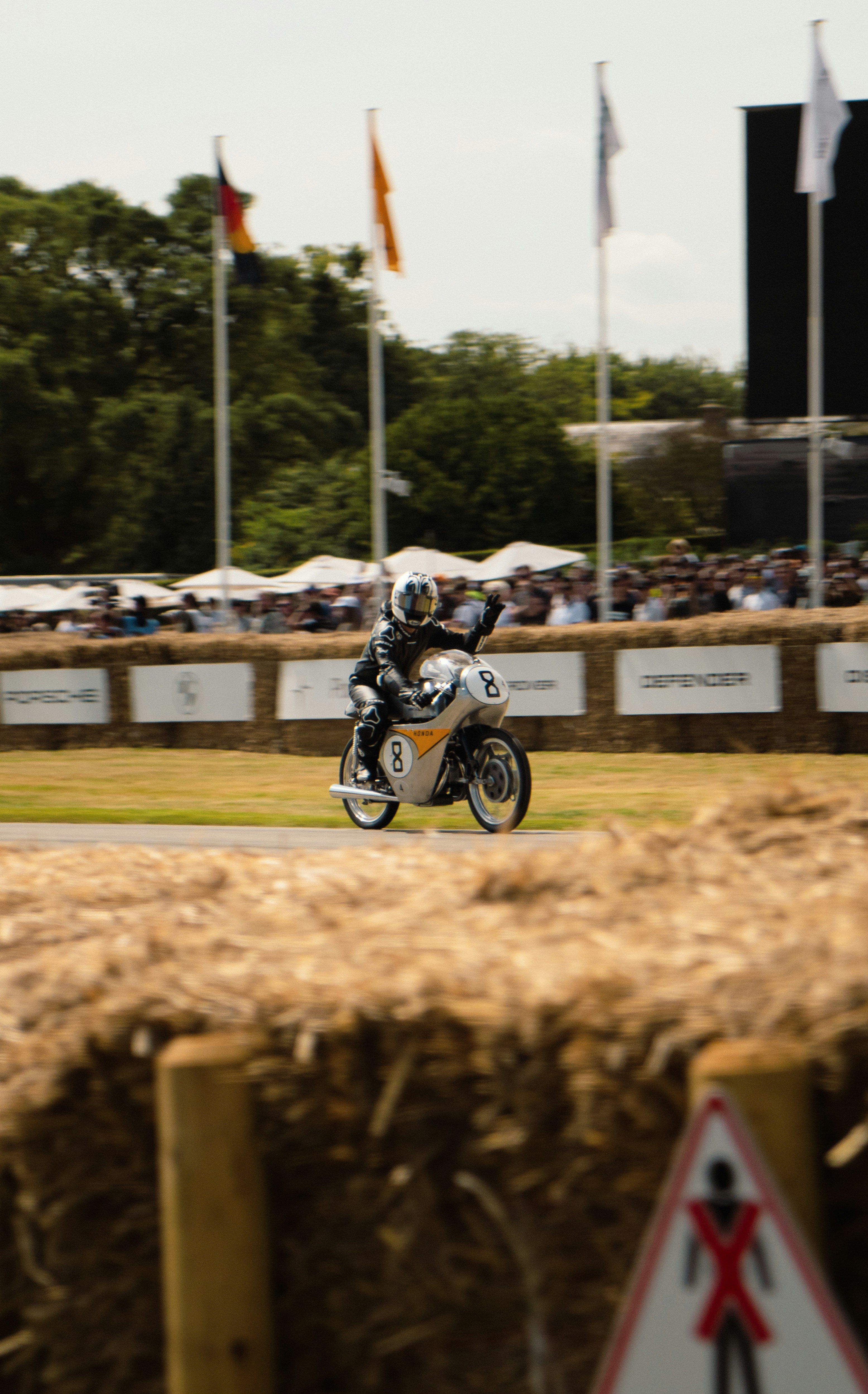 Piloto en motocicleta vintage olas durante una carrera.