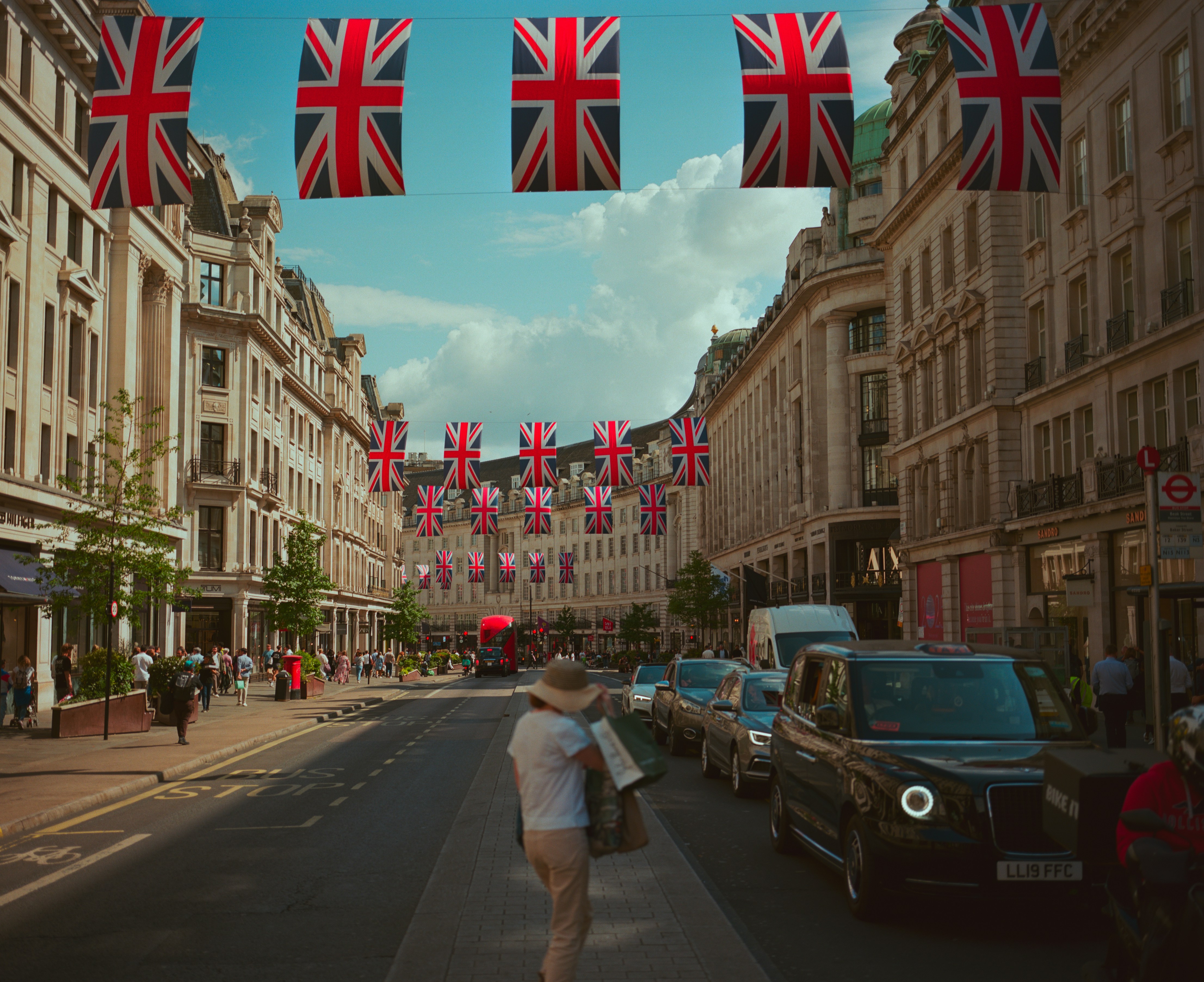Regent Street in London on a sunny afternoon, adorned with Union Jack flags, exuding a lively atmosphere.
