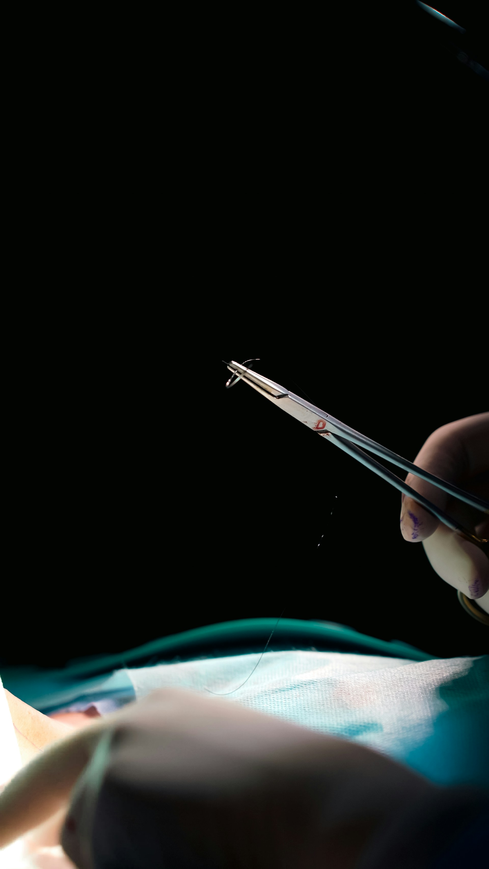 Surgeon holding surgical instrument with dark background.