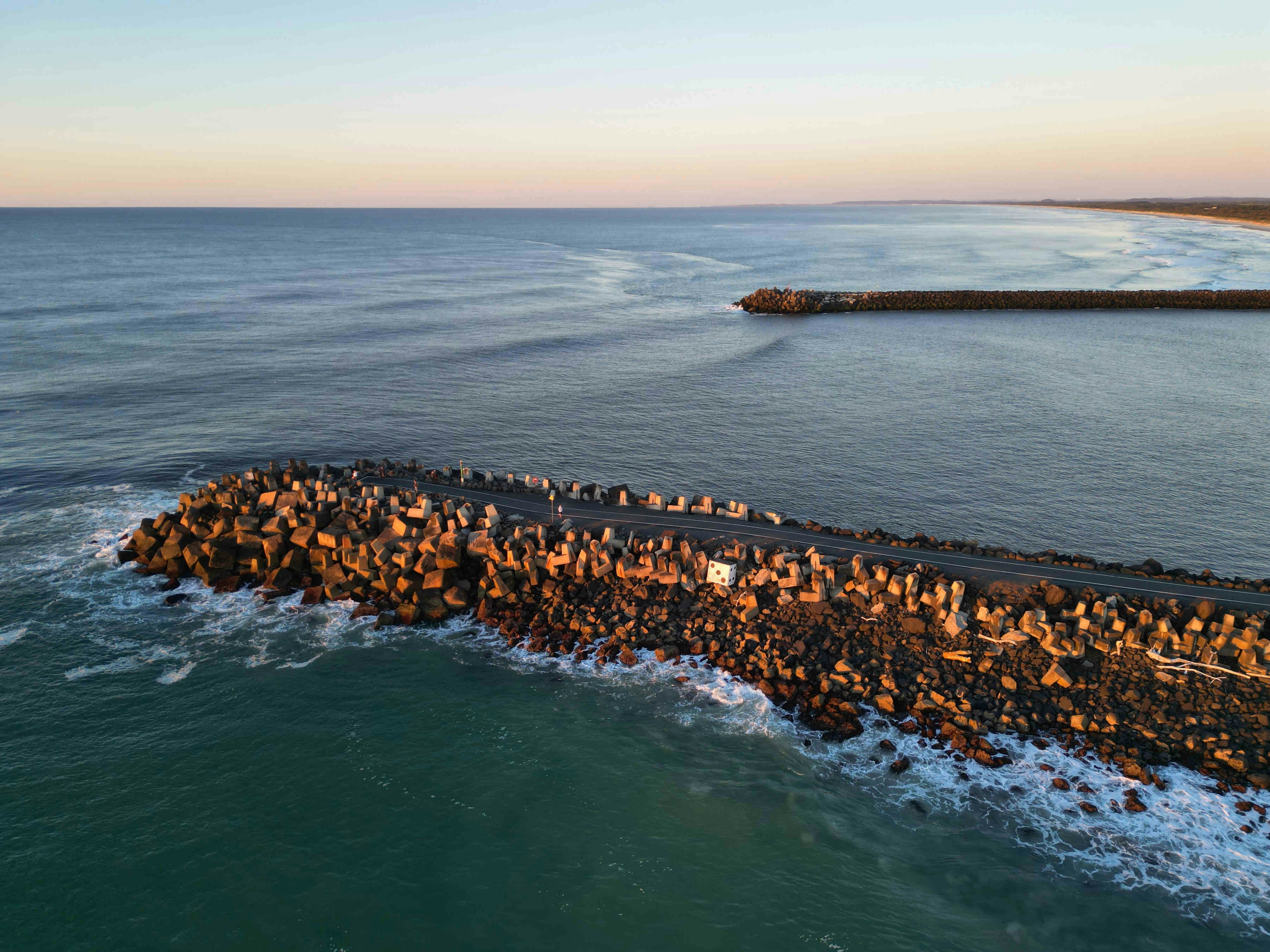 Stone breakwater extends into the ocean at sunset.