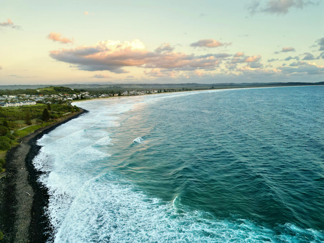 The coastal town of Lennox Head with waves rolling in and hills beyond