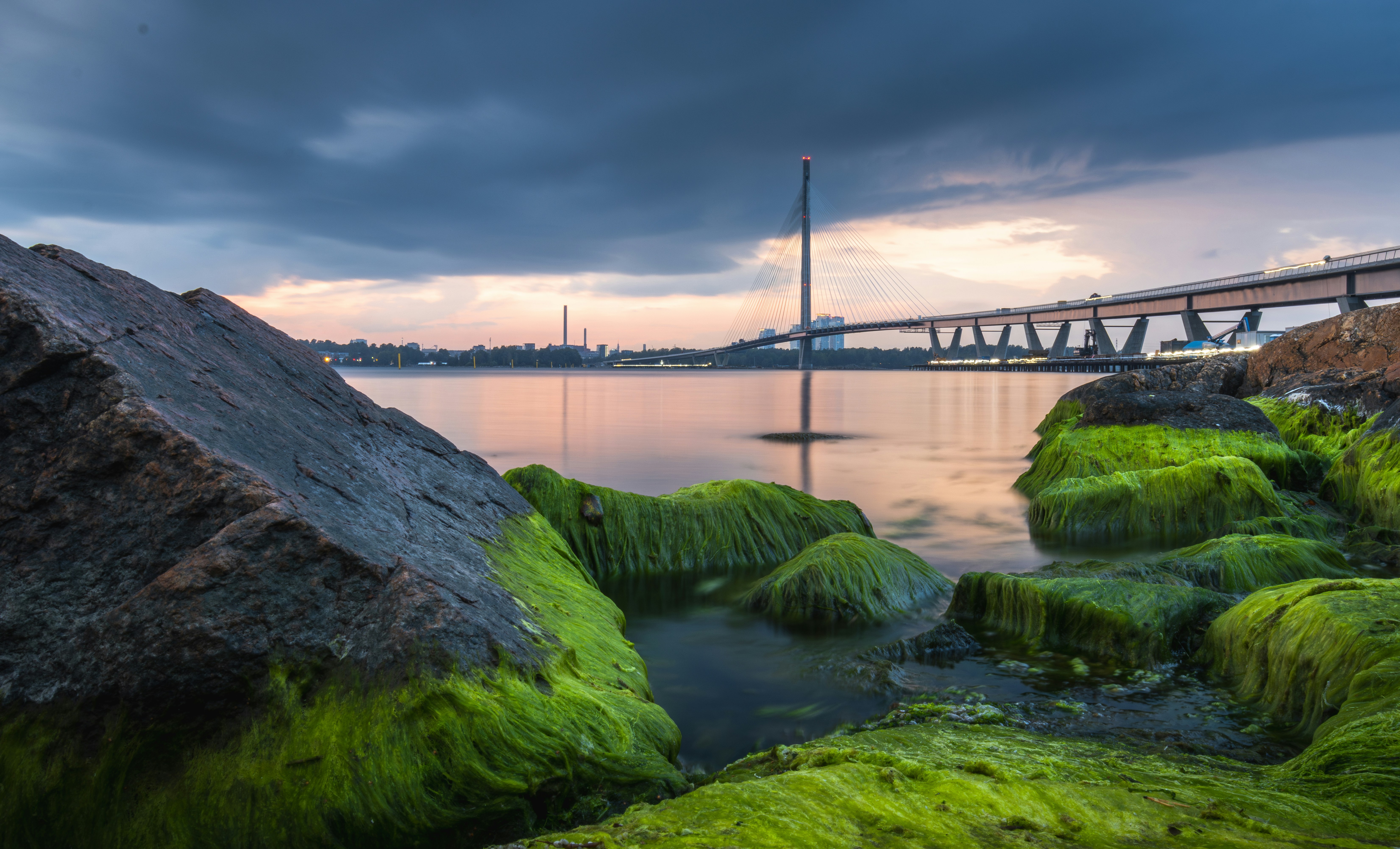 Mossy rocks by a calm bay with a bridge.