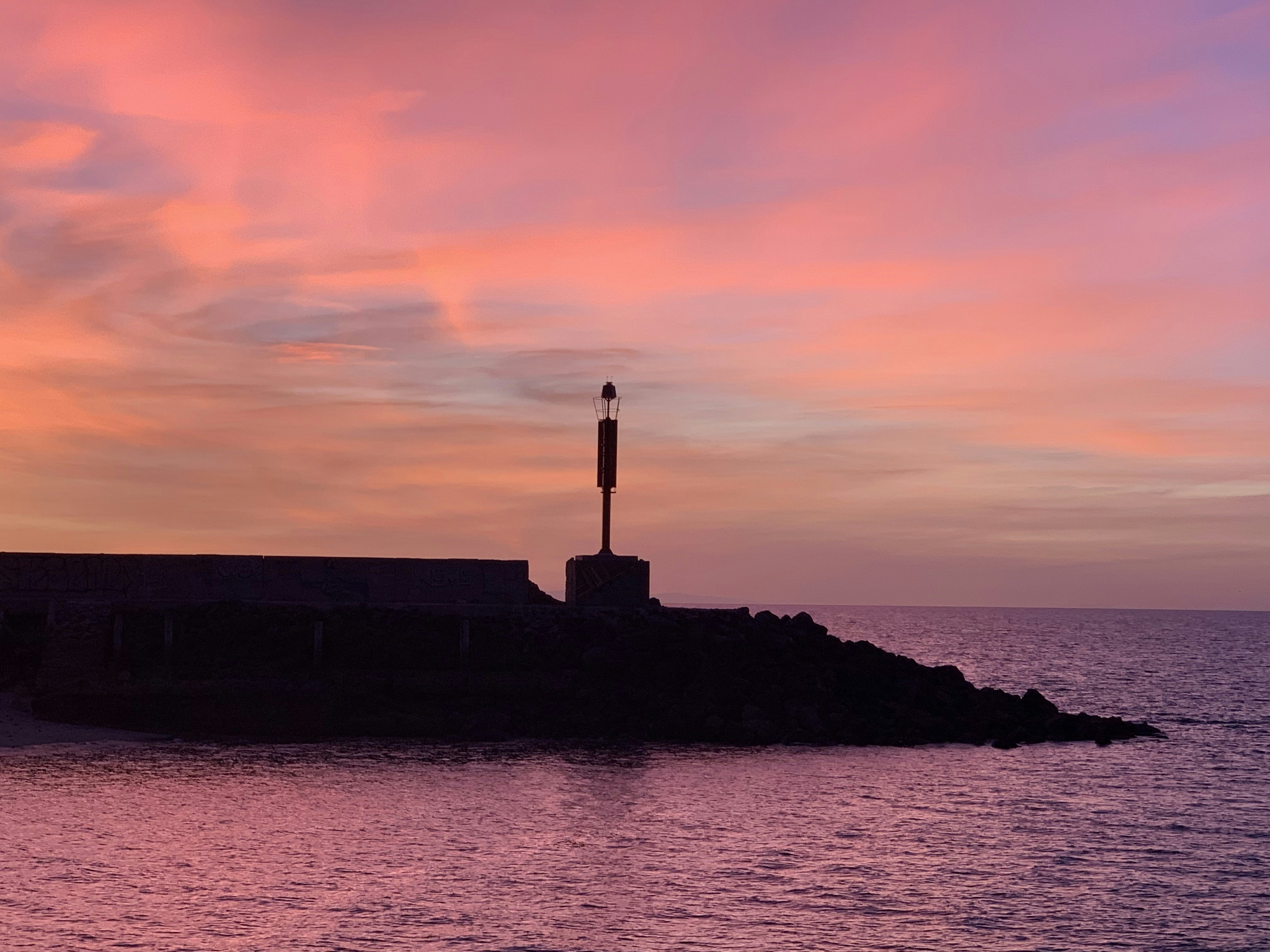 Silhouette of a lighthouse at sunset with pink sky.
