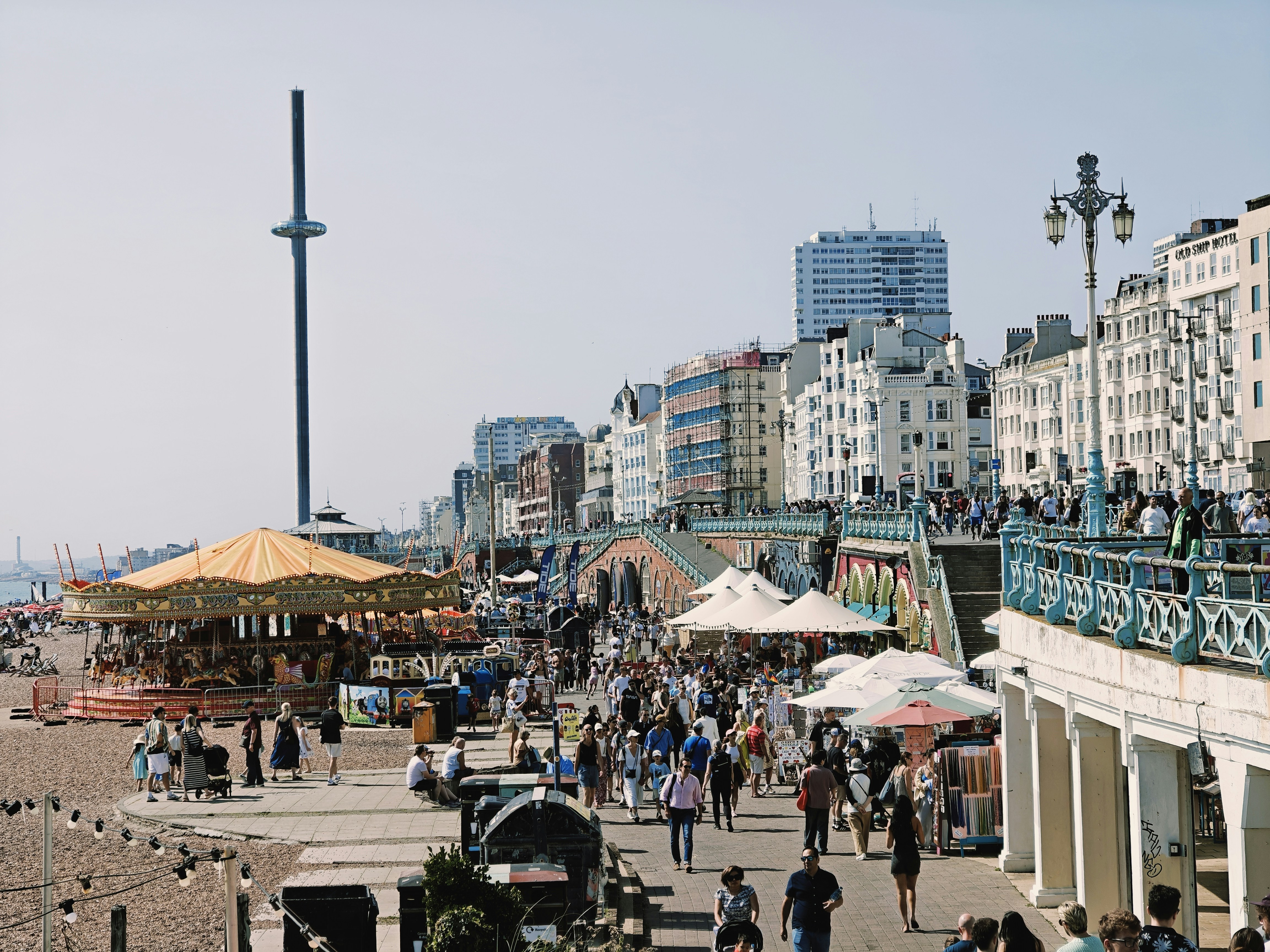 People strolling along a sunny beachfront promenade with buildings.
