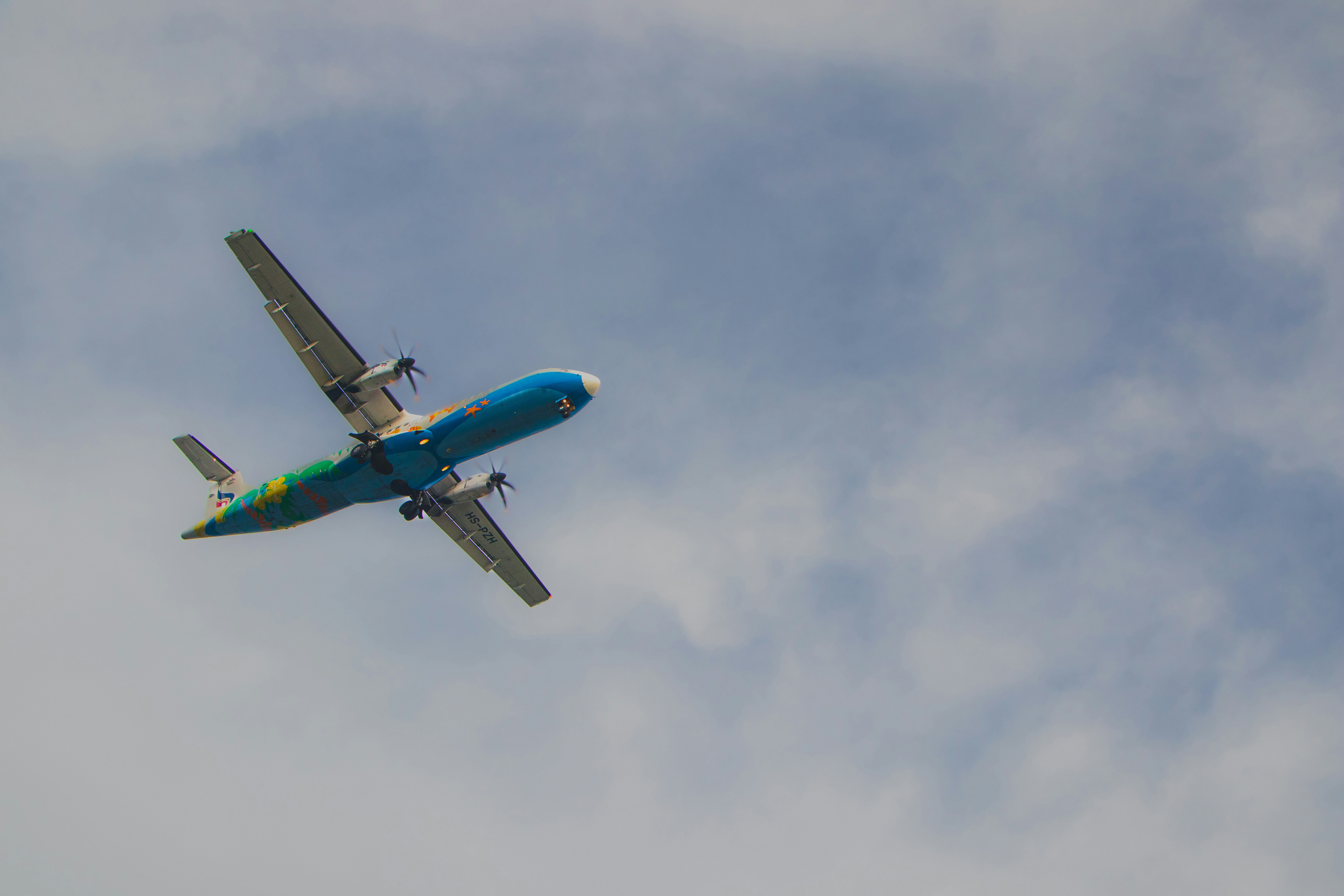 A blue airplane flying in a cloudy sky.