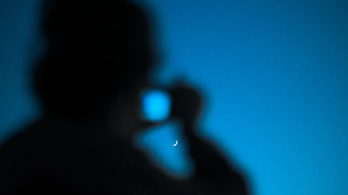 Siluet seseorang memegang ponsel dengan bulan di langit