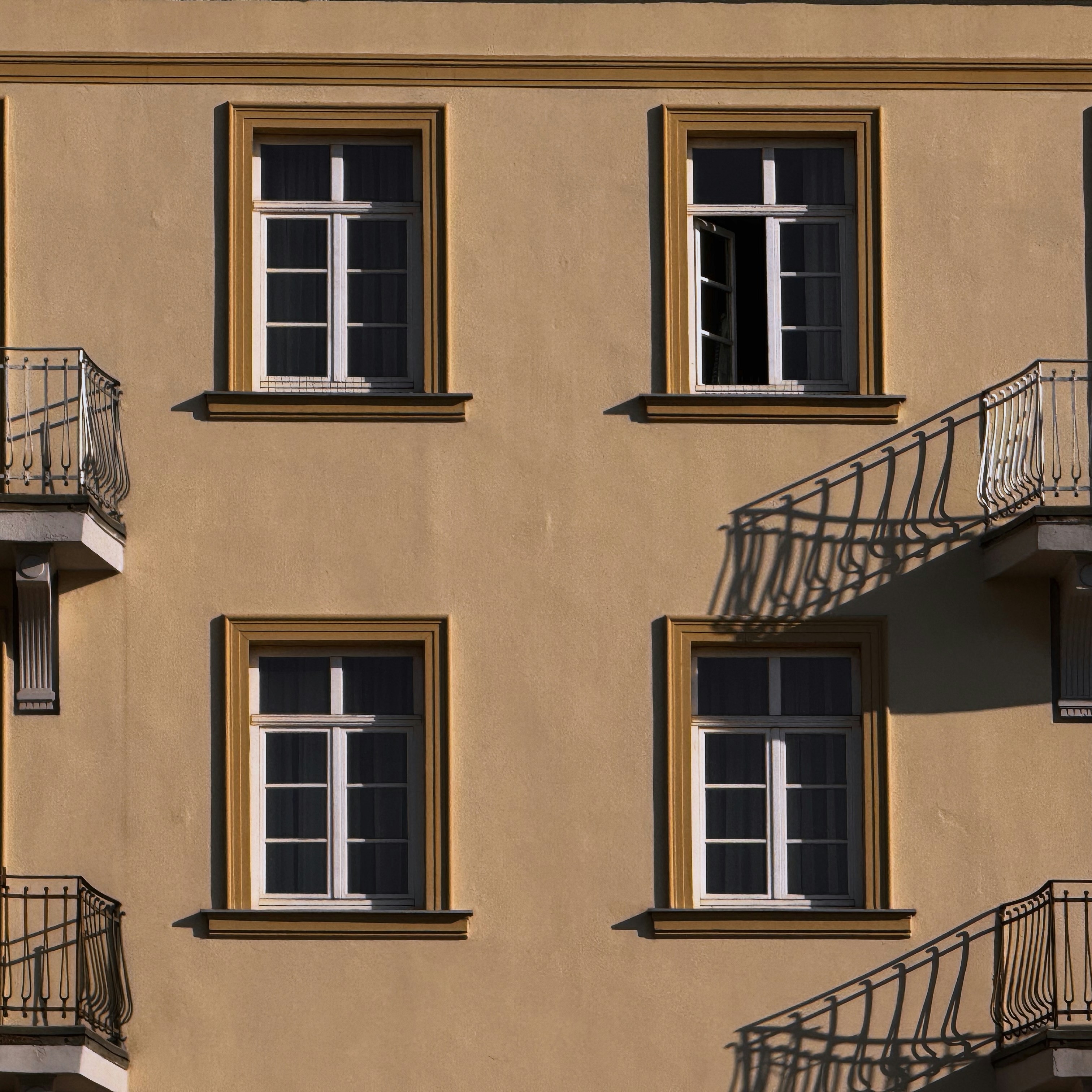 Vier Fenster und Balkone an einem beigen Gebäude