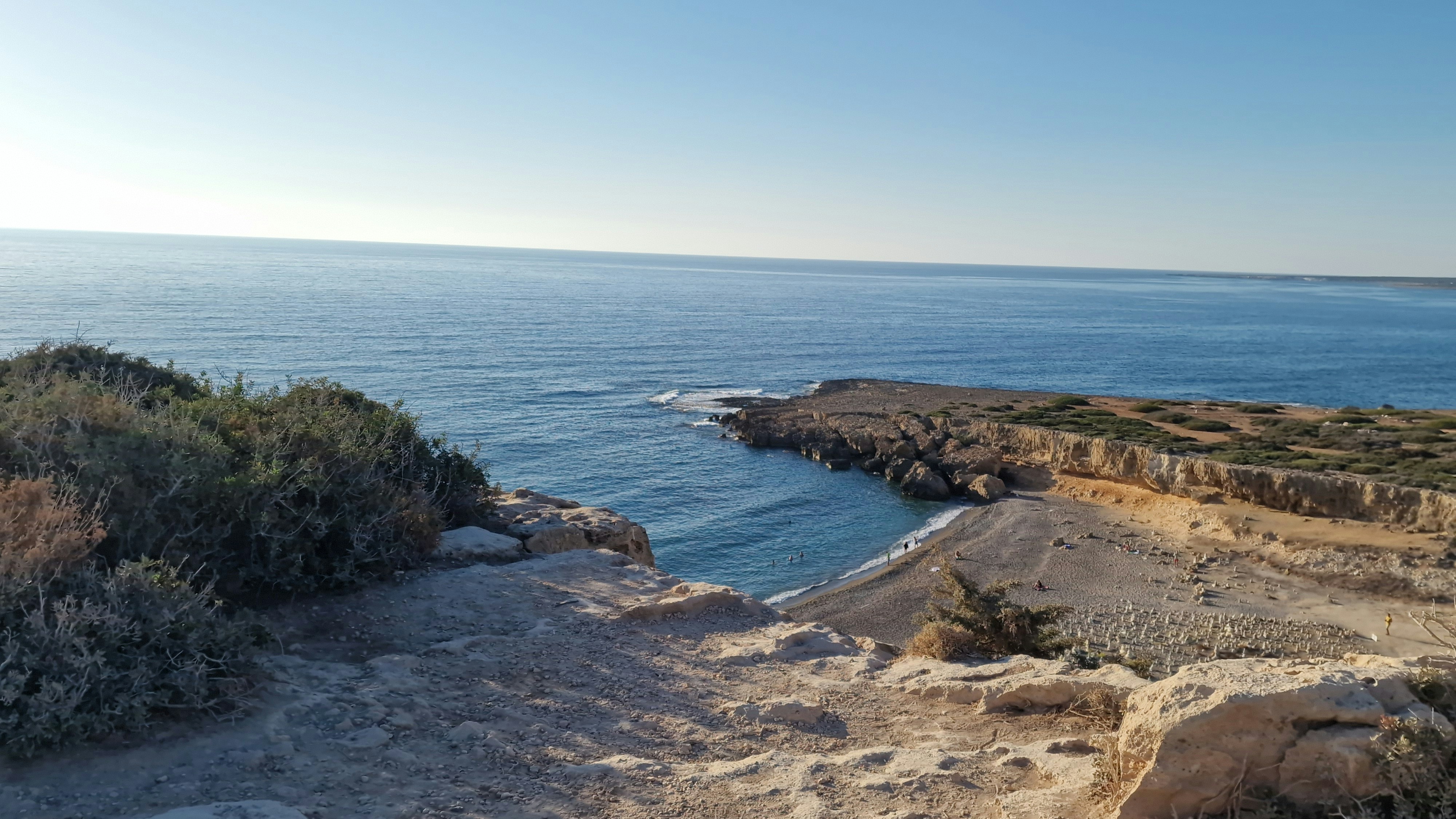 Rocky coastline with calm blue ocean waters and clear sky.