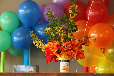 Colorful balloons and a vibrant flower arrangement on a shelf.