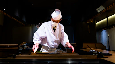 A sushi chef preparing pieces at a restaurant counter