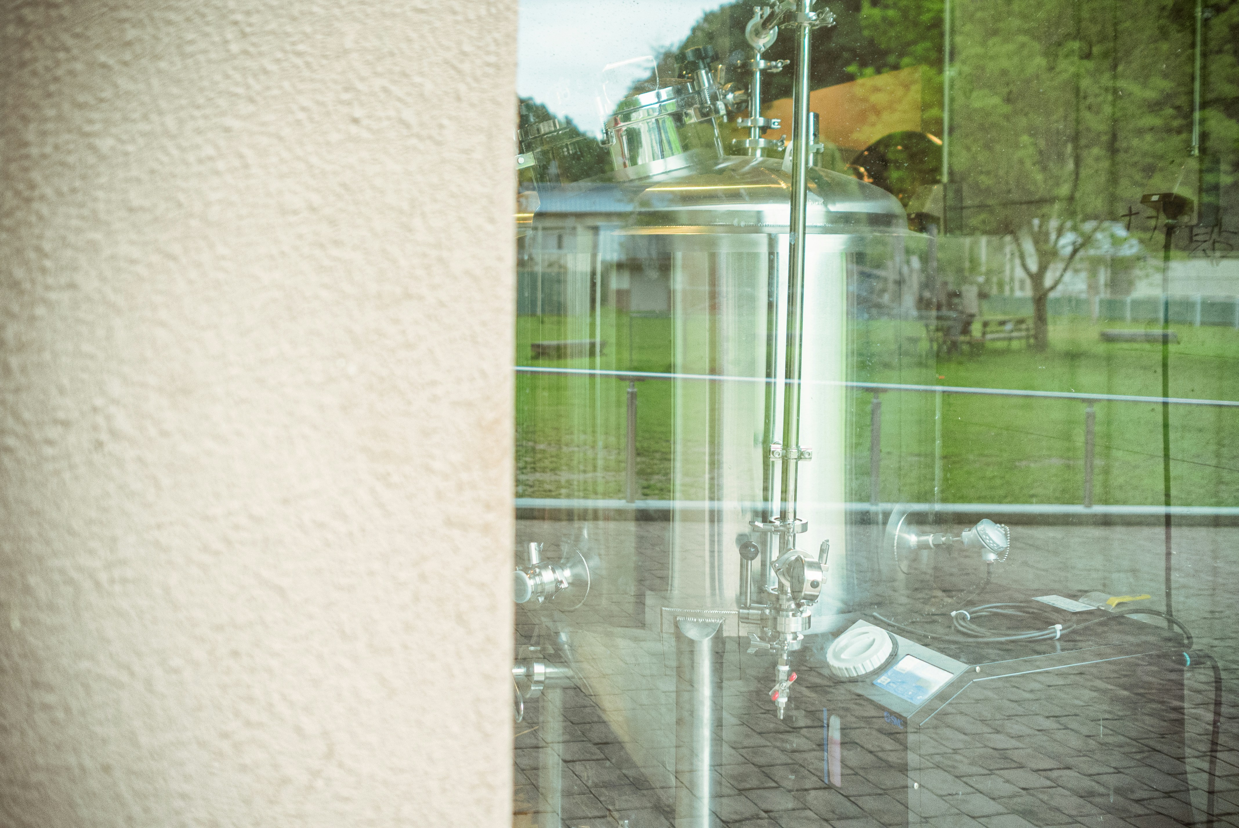 Stainless steel tanks reflected in window with trees outside
