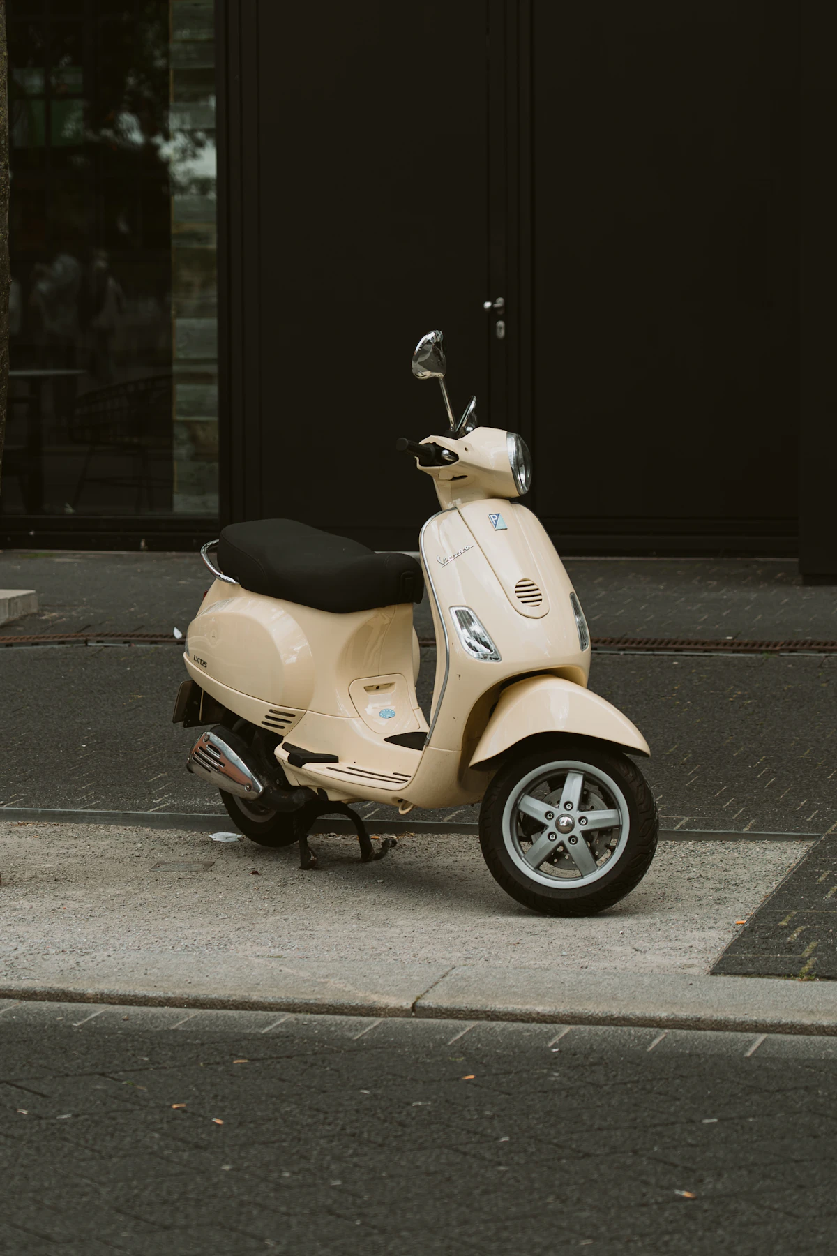 Cream colored vintage Vespa scooter parked on sidewalk