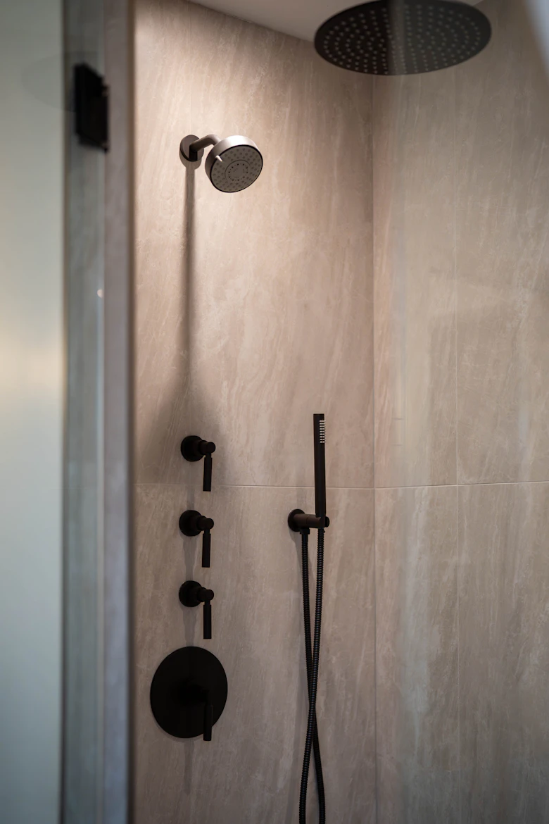 Black rainfall shower and controls against warm stone-effect tiles — illustrative stock photograph