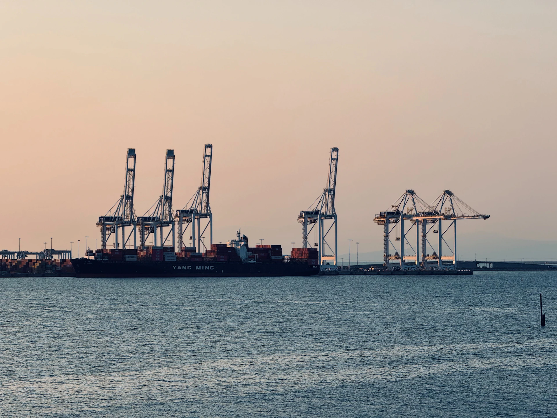 Cargo ship and cranes at a harbor during sunset.