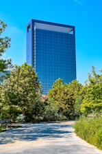 Modern glass skyscraper surrounded by lush green trees.