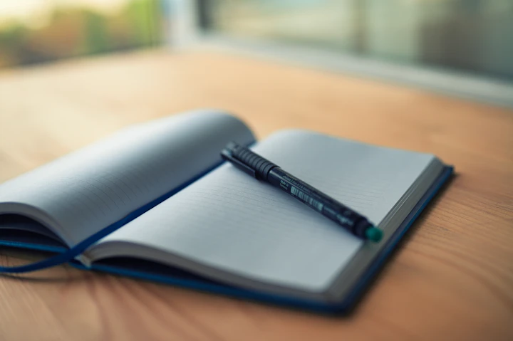 Illustrative scene: An open notebook and pen on a wooden table. Not a photograph of The Five Minute Journal.