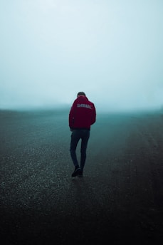 Man in red hoodie walks on misty road