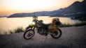 Motorcycle parked on a cliff overlooking the ocean at sunset.