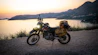 Motorcycle parked on a cliff overlooking the ocean at sunset.