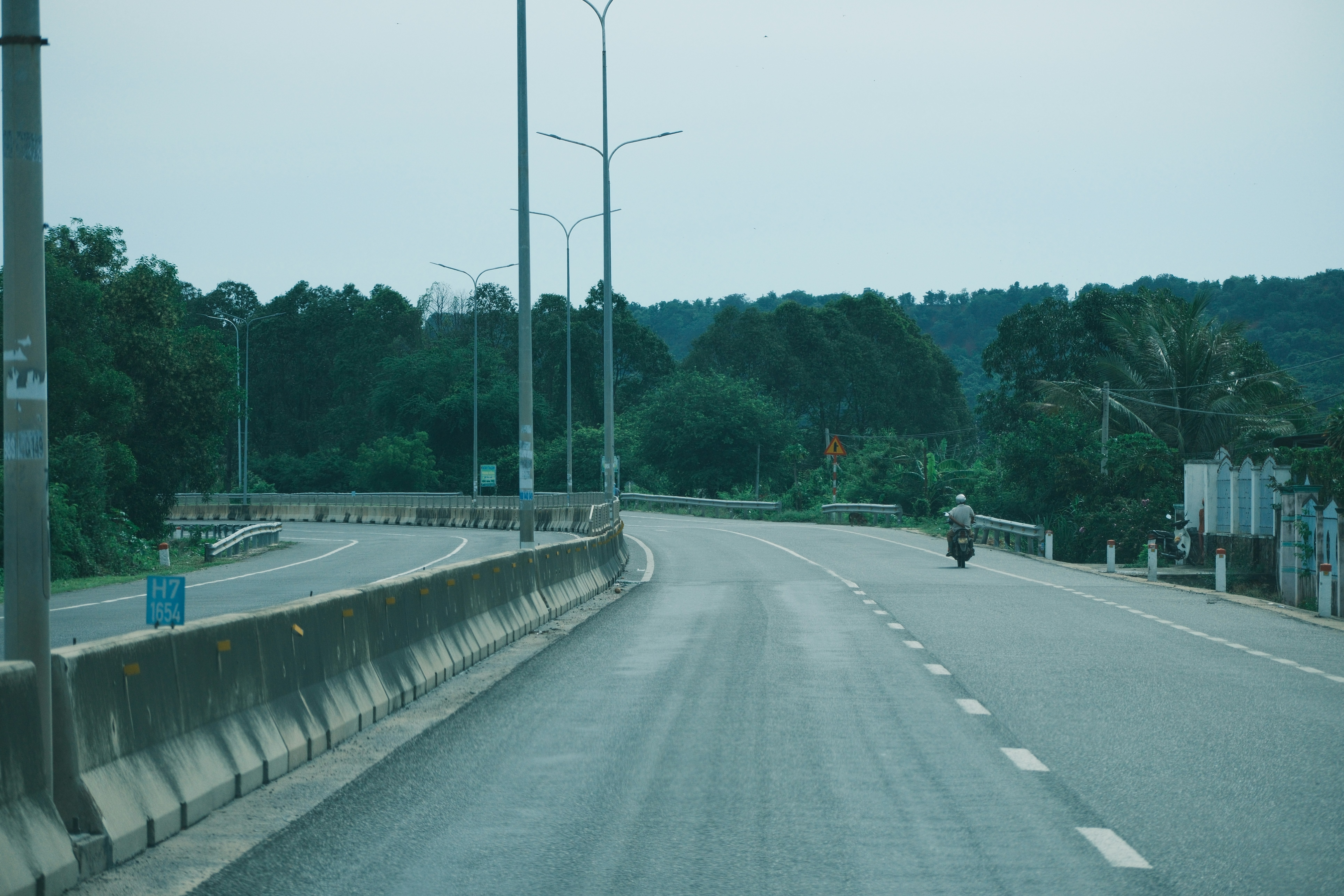 Motorcyclist on a road with trees and overcast sky