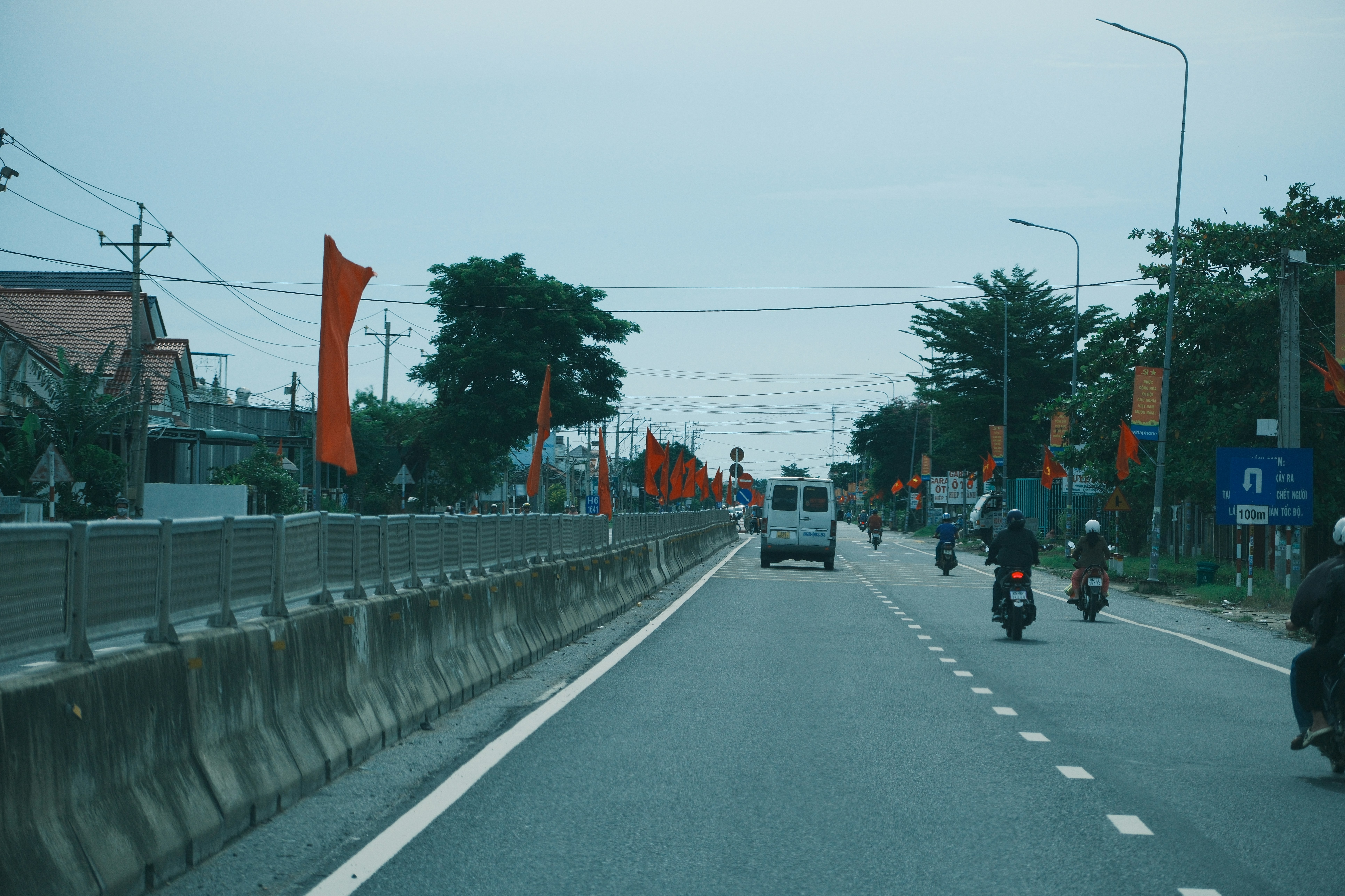 Orange flags line a road with vehicles and trees.