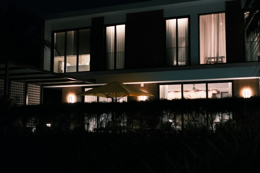 Modern two-storey house at night with warm lit windows behind dark foliage