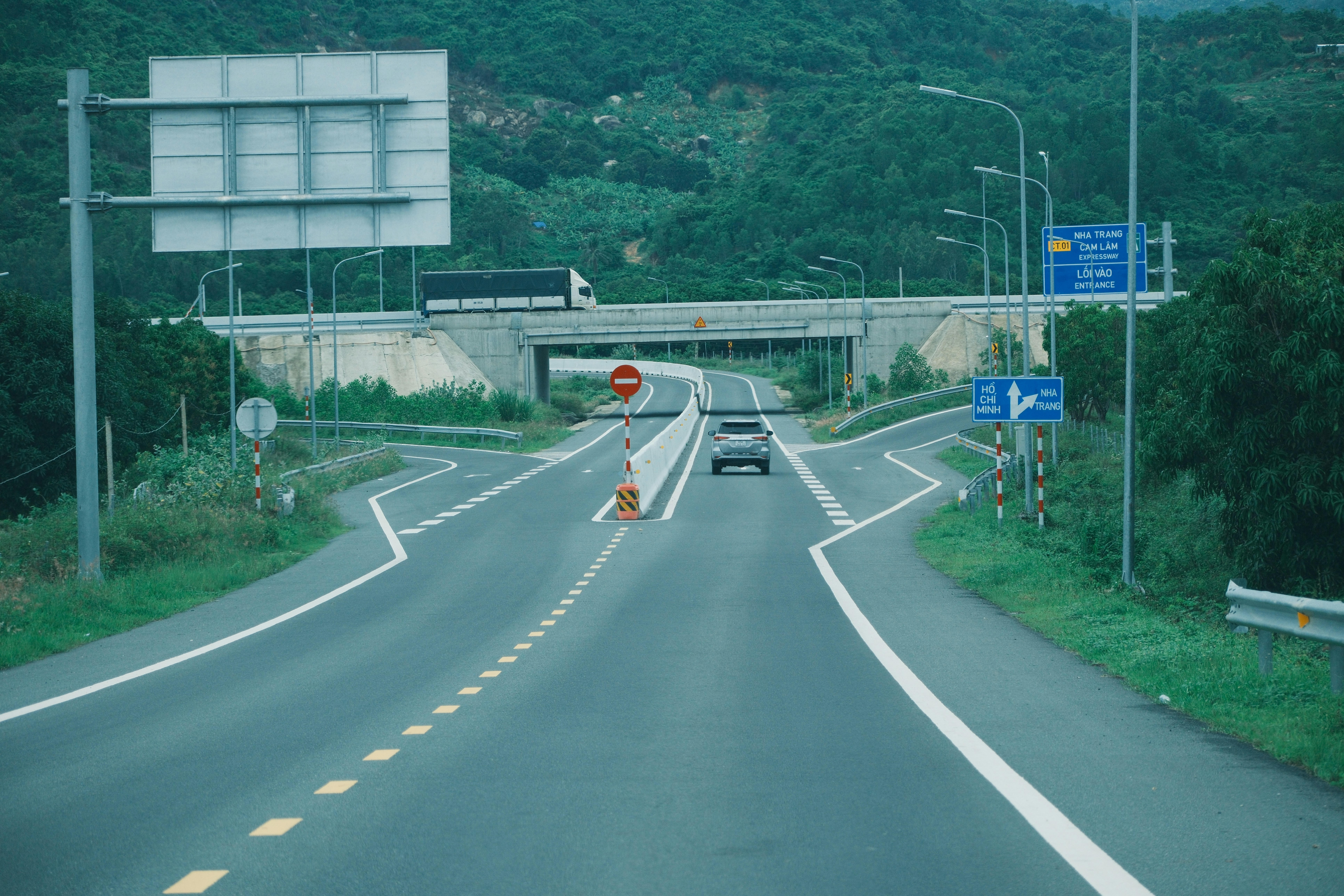 Cars drive on a highway under an overpass.