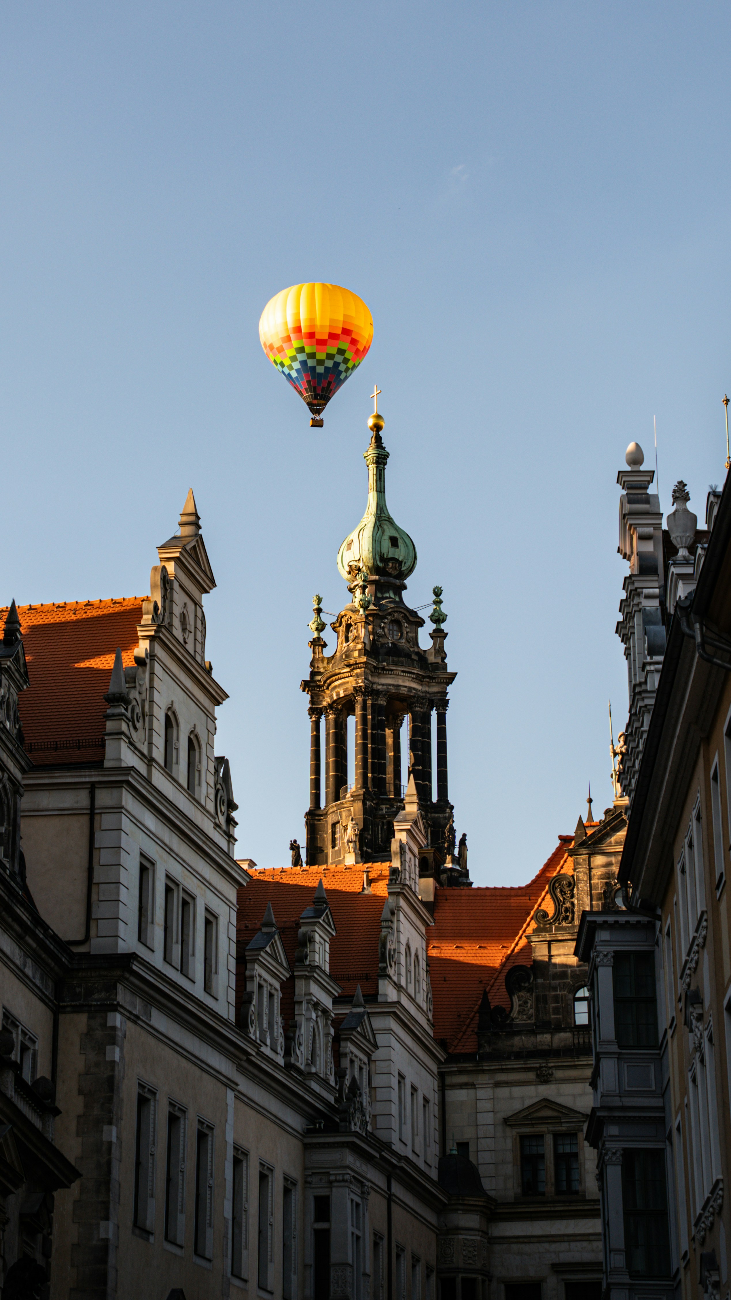 A colorful hot air balloon flies over historic european architecture.
