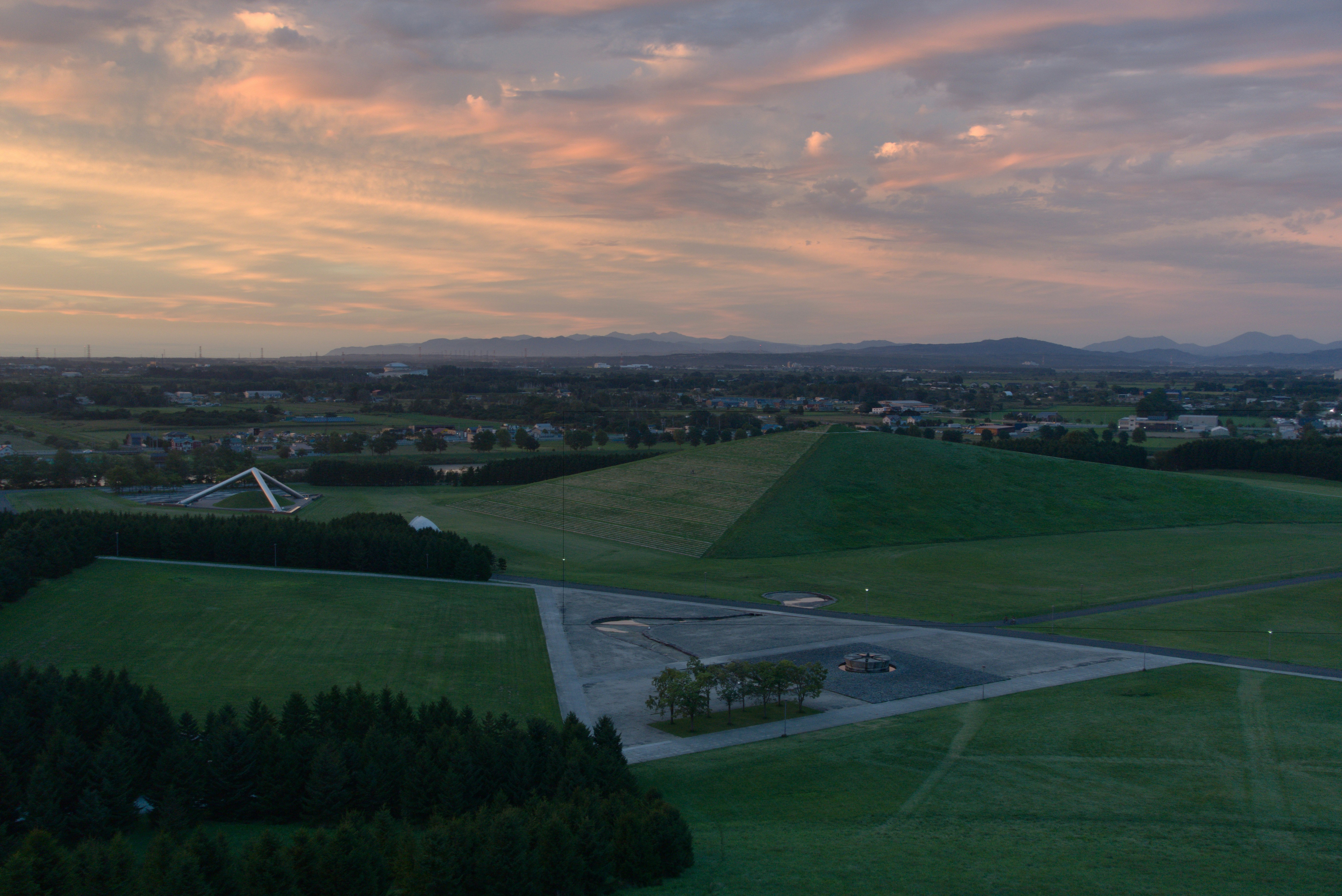 Sunset over green fields with distant mountains.