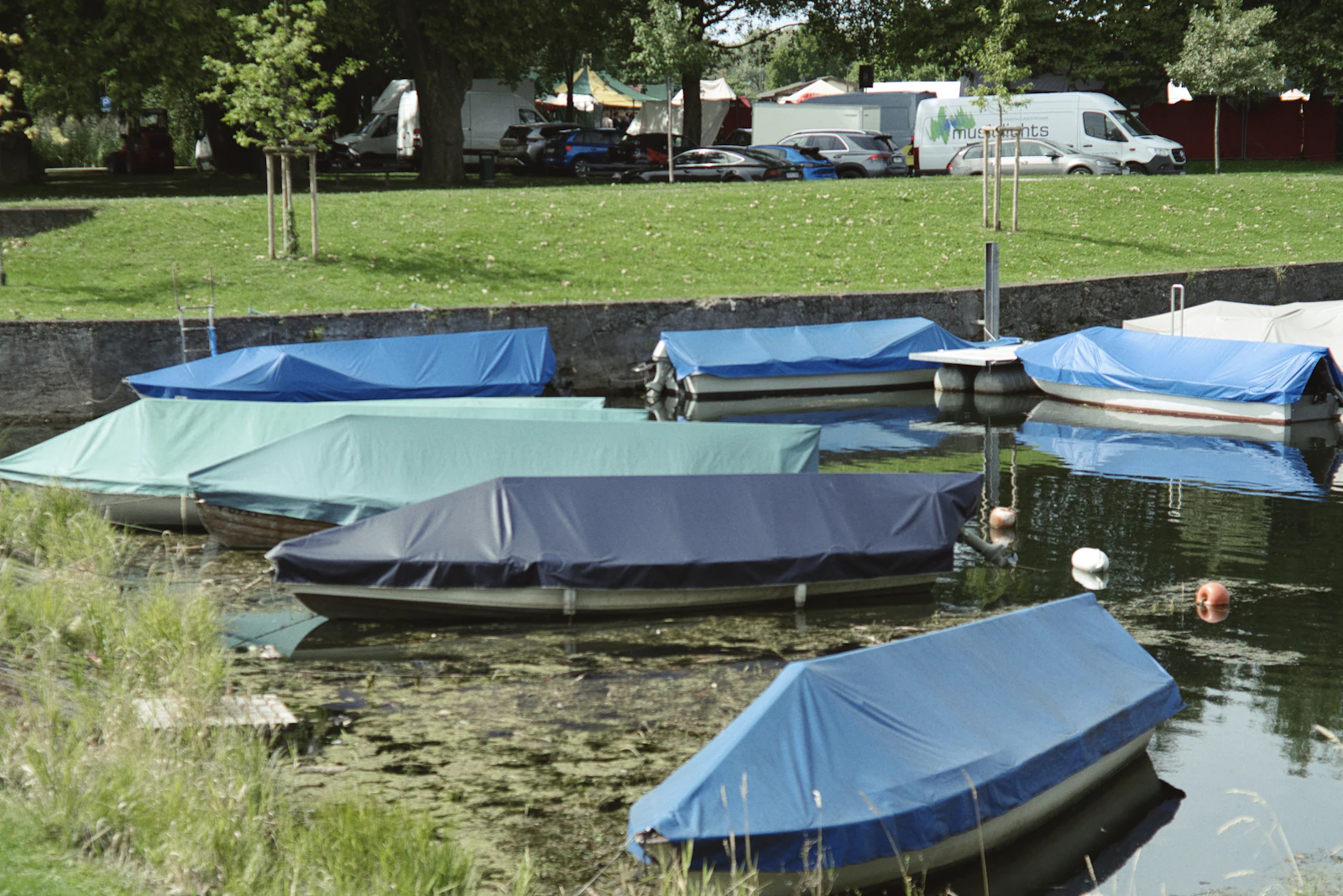 Boats under covers moored along a calm inland lake.