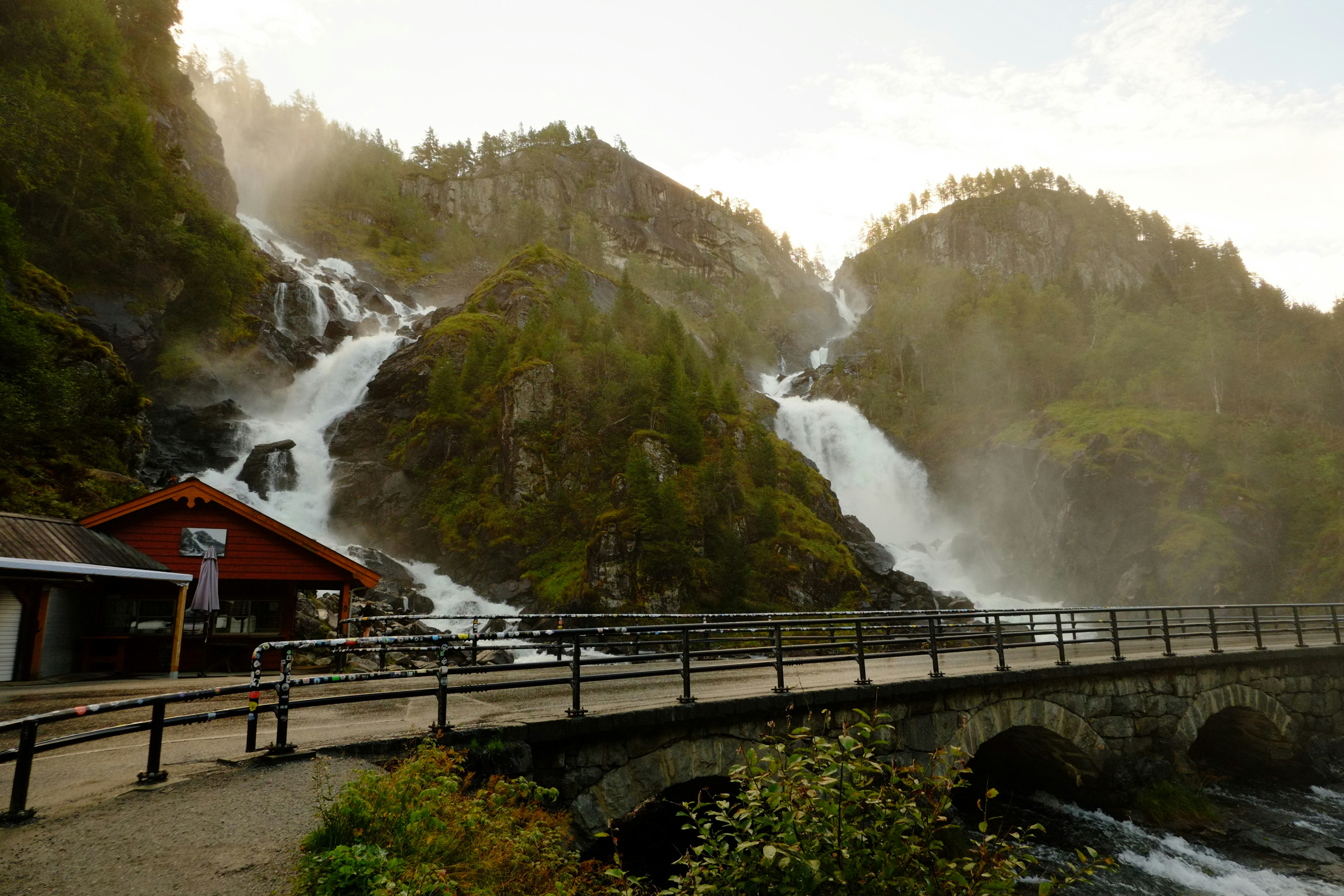 Majestic waterfalls cascade down rocky cliffs near a bridge.