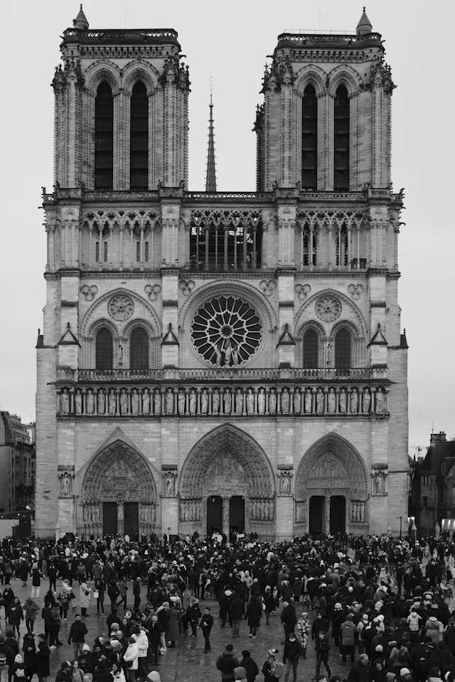 Black-and-white view of Notre-Dame cathedral's twin towers and rose window with a crowd gathered in the square below