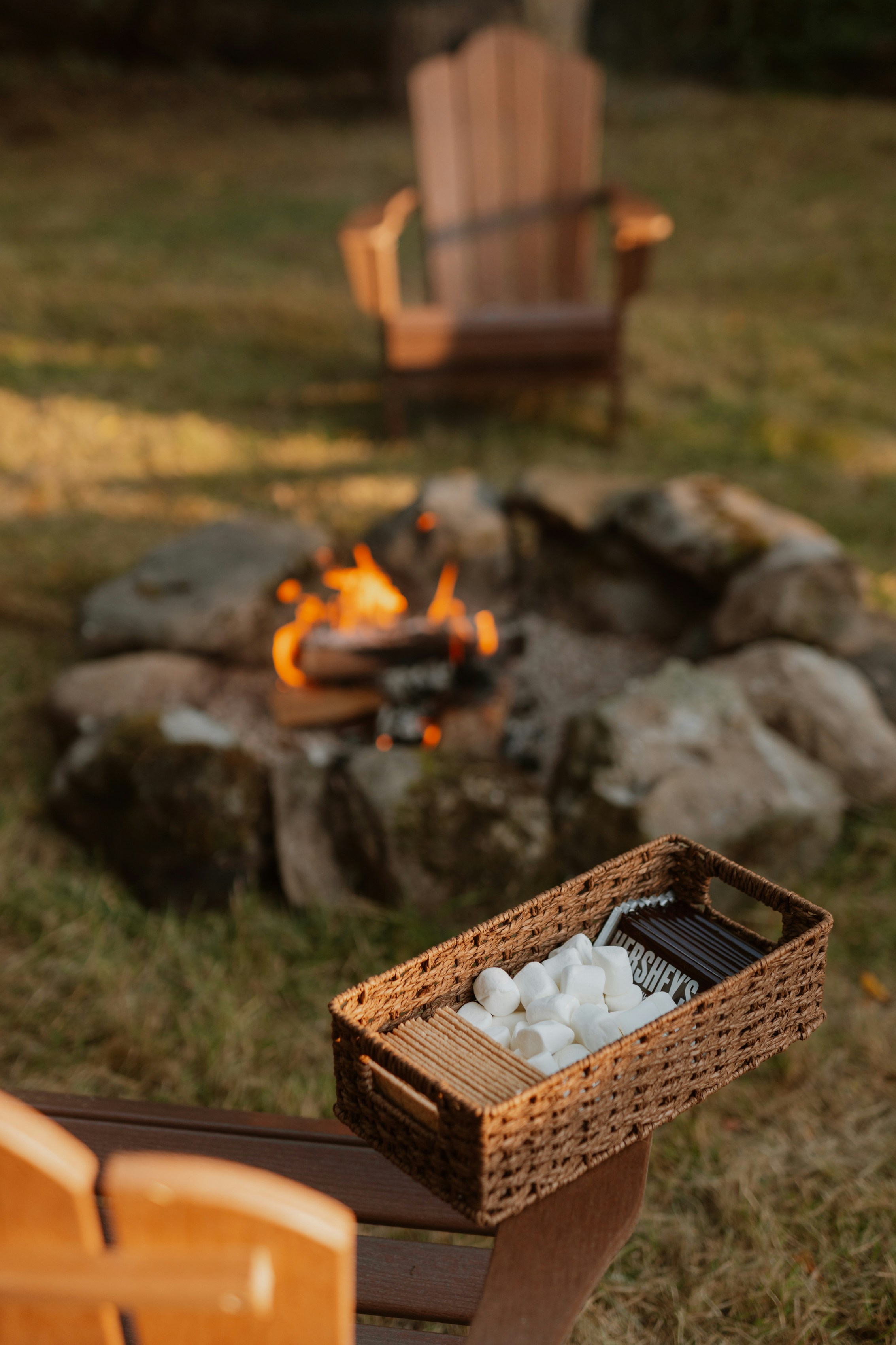 S'mores ingredients beside a campfire with chairs.