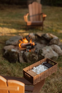 S'mores ingredients beside a campfire with chairs.