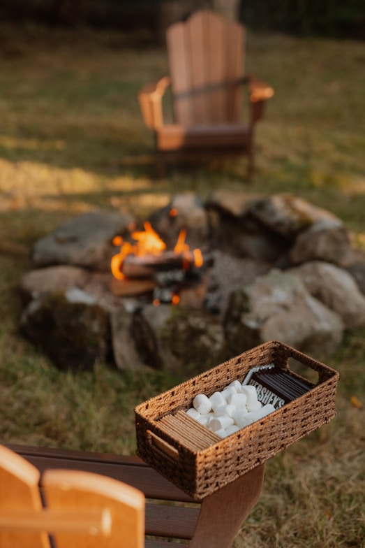 S'mores ingredients beside a campfire with chairs.