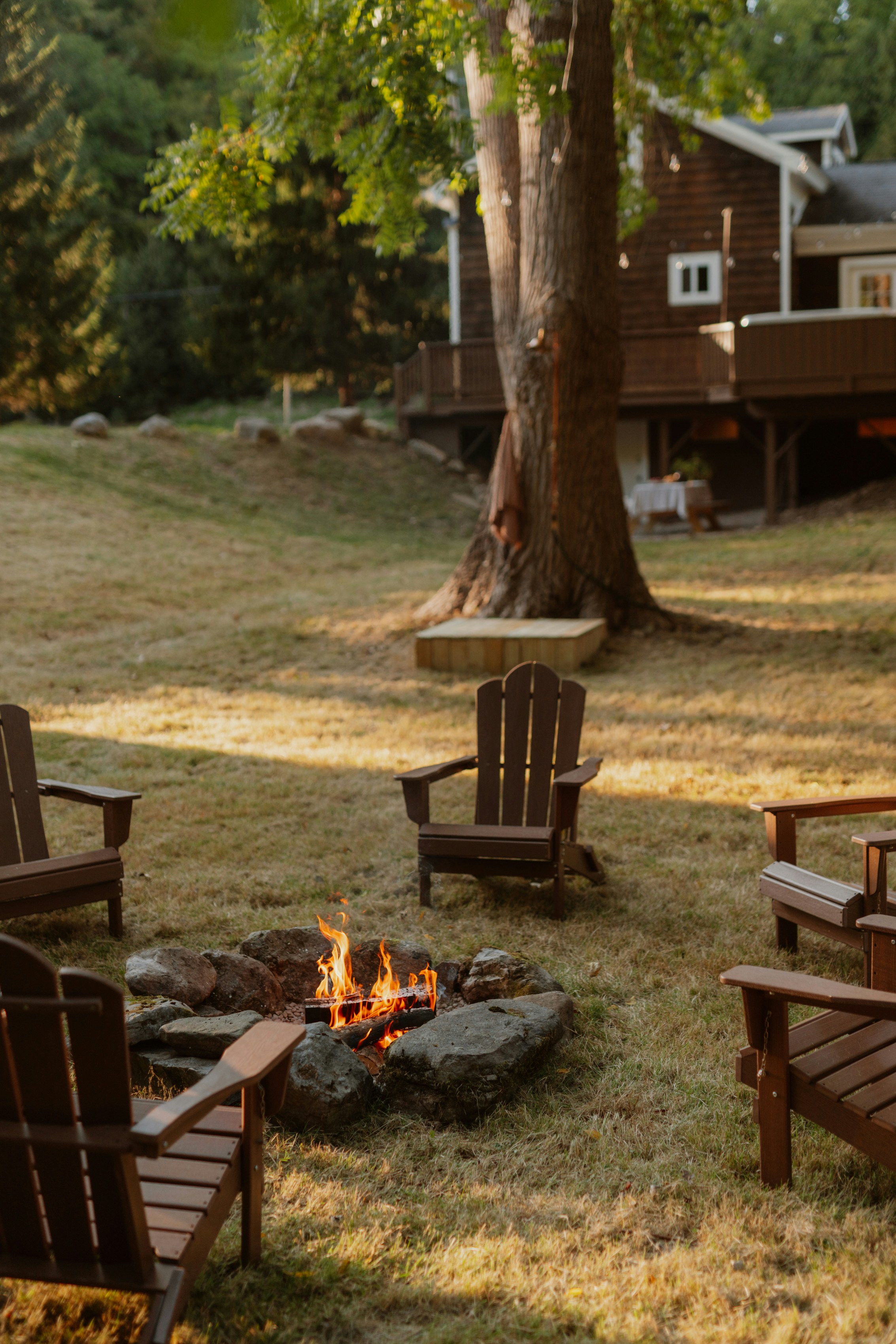 Adirondack chairs surround a lit fire pit in a backyard.