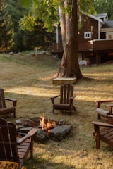 Adirondack chairs surround a lit fire pit in a backyard.
